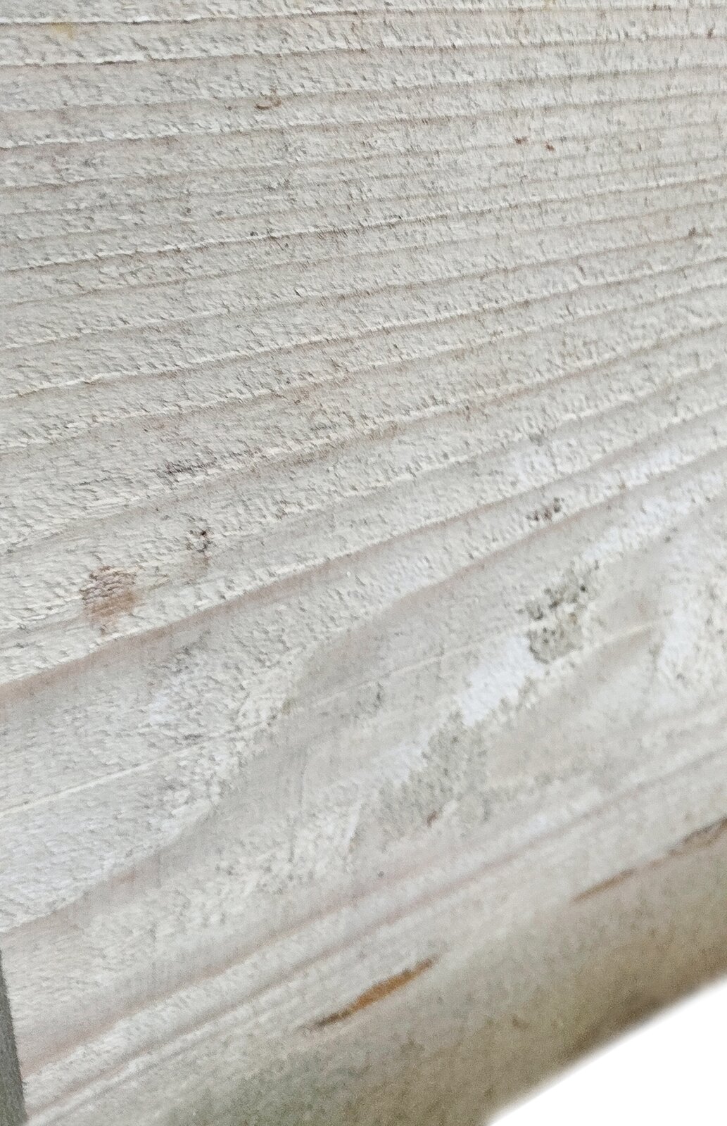 Zdjęcie przedstawia deskę świerkową. Widoczny jest fragment jasnobrązowej deski, w pionie, na powierzchni której widoczne są jasnoszare słoje drewna oraz poziome linie obrazujące strukturę drewna po obróbce.