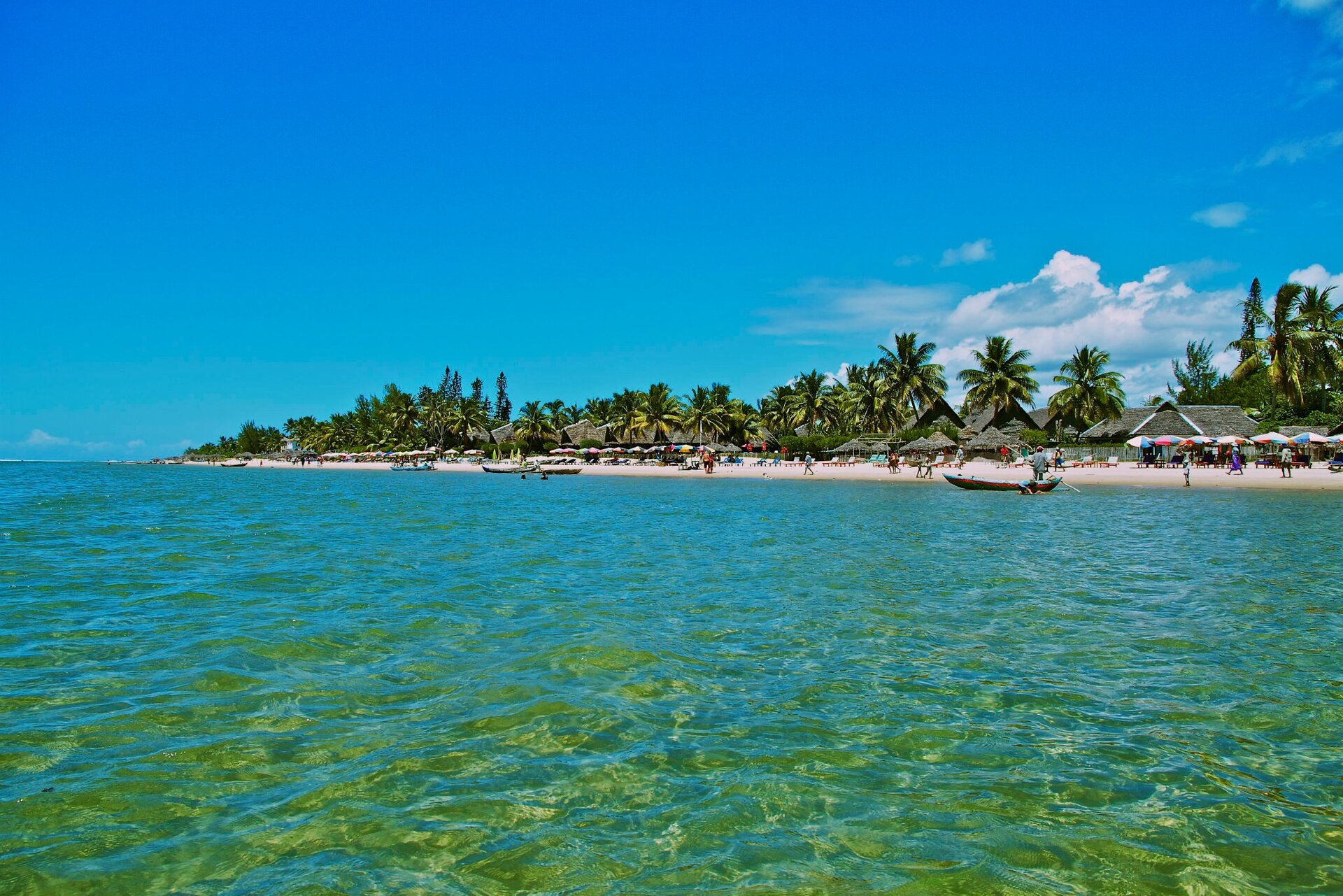 Na zdjęciu na pierwszym planie morze, dalej brzeg morza, piaszczysta plaża, palmy, zabudowania z dachami krytymi słomą lub palmowymi liśćmi.