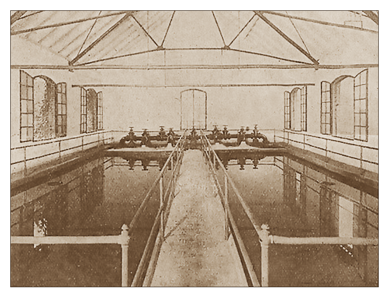 Zdjęcie przedstawia halę filtrów tczewskich wodociągów. Po prawej i lewej stronie fotografii widoczne są baseny z napływającą i odprowadzającą wodą. Pośrodku hali jest pomost ograniczony barierkami. Pomost prowadzi do systemu ciemnych rur i kranów.