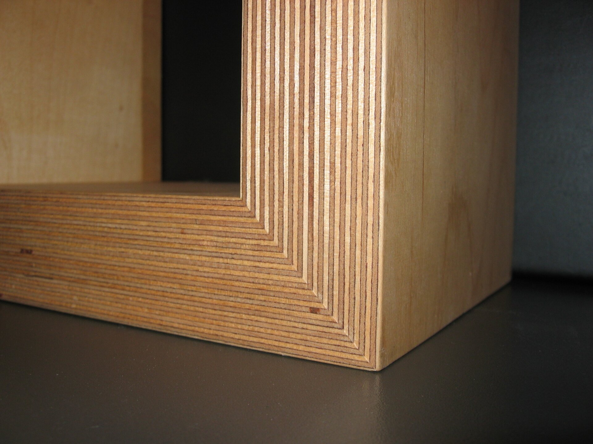 Zdjęcie przedstawia zbliżenie na element wykonany ze sklejki. Sklejka to materiał składający się ze sklejonych ze sobą cienkich warstw drewna. Pojedyncze warstwy sklejki są rozróżnialne. 