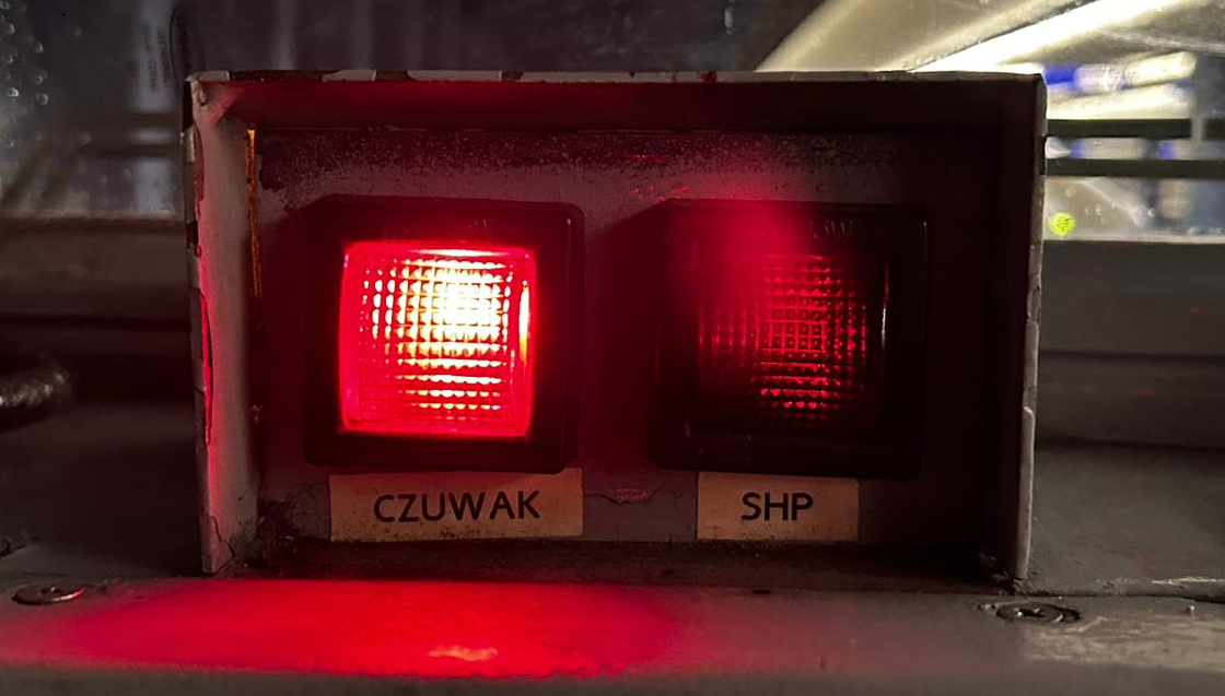 Zdjęcie przedstawia wskaźnik czuwaka aktywnego. Są to dwie lampki w skrzynce. Pierwsza lampka świeci na czerwono a pod nią znajduję się napis czuwak, druga lampka jest wyłączona i znajduje się pod nią napis SHP. Lampki są w kształcie kwadratów. 