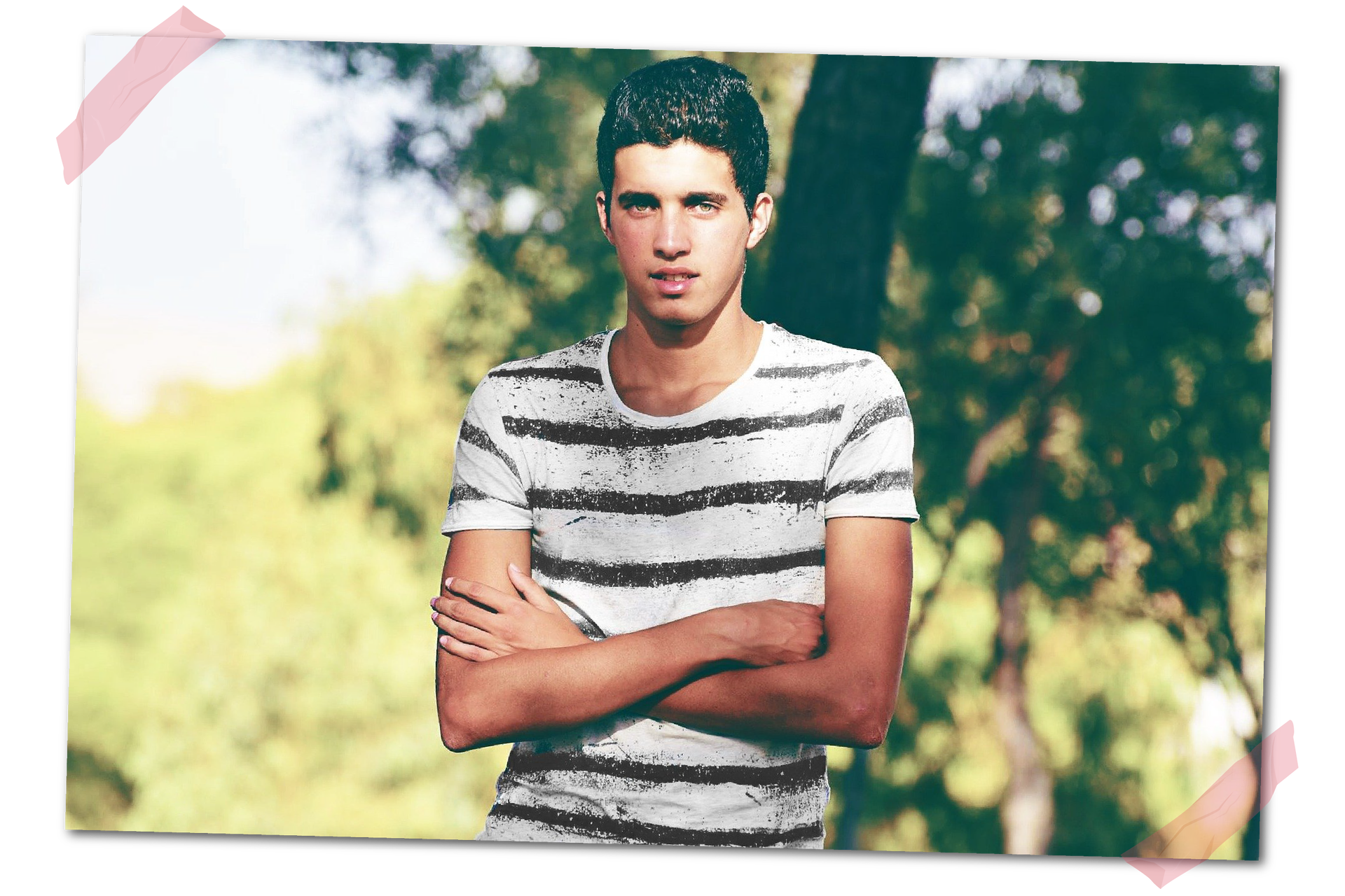 Zdjęcie nastolatka stojącego z założonymi rękami na tle drzew.