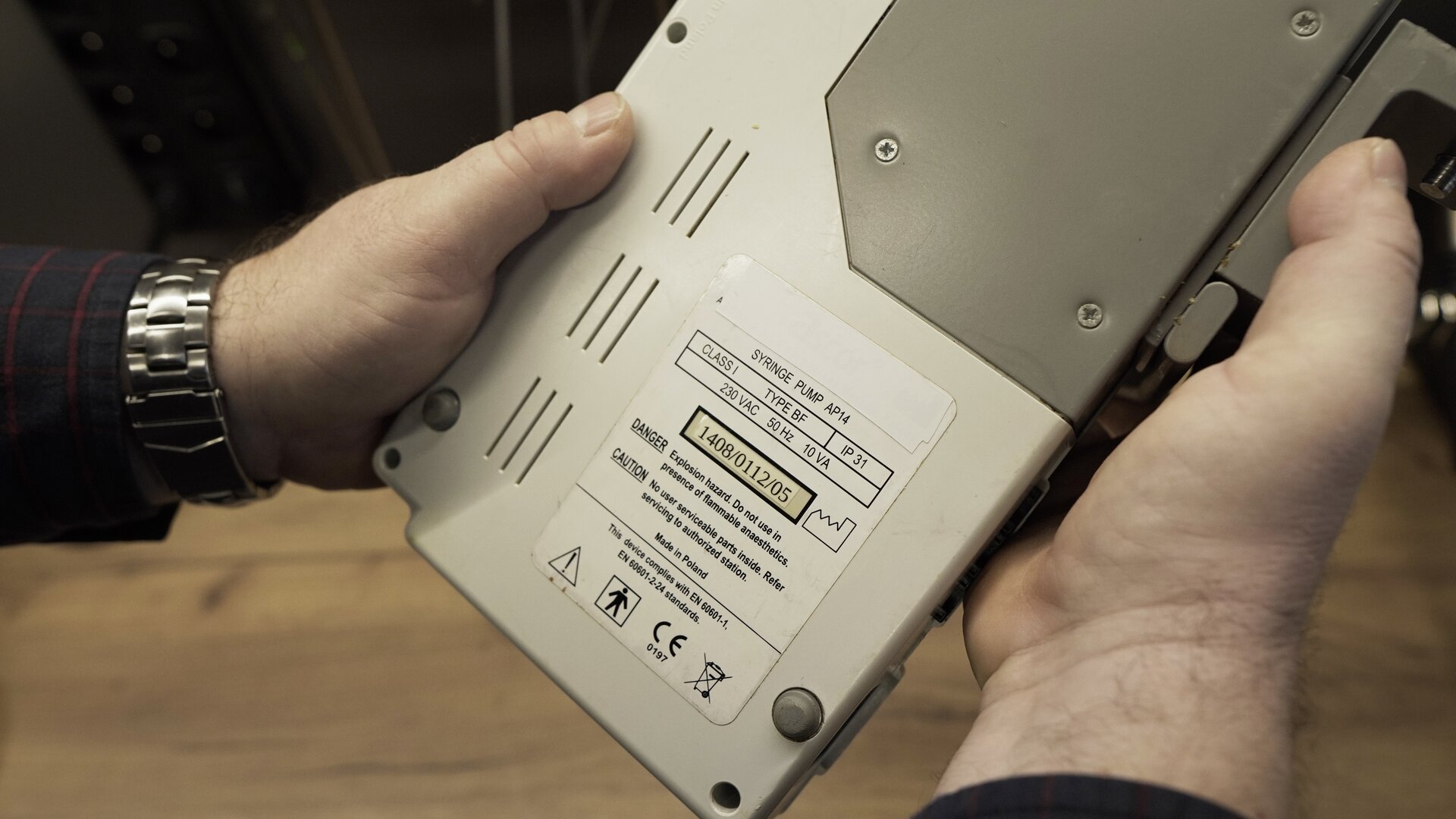 Zdjęcie przedstawia zbliżenie na tabliczkę znamionową umieszczoną na spodzie obudowy pompy infuzyjnej. 