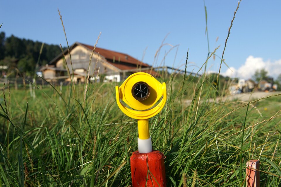 Na zdjęciu jest urządzenie stojące w trawie. Na krótkiej rurce zamontowane jest okrągłe urządzenie.  