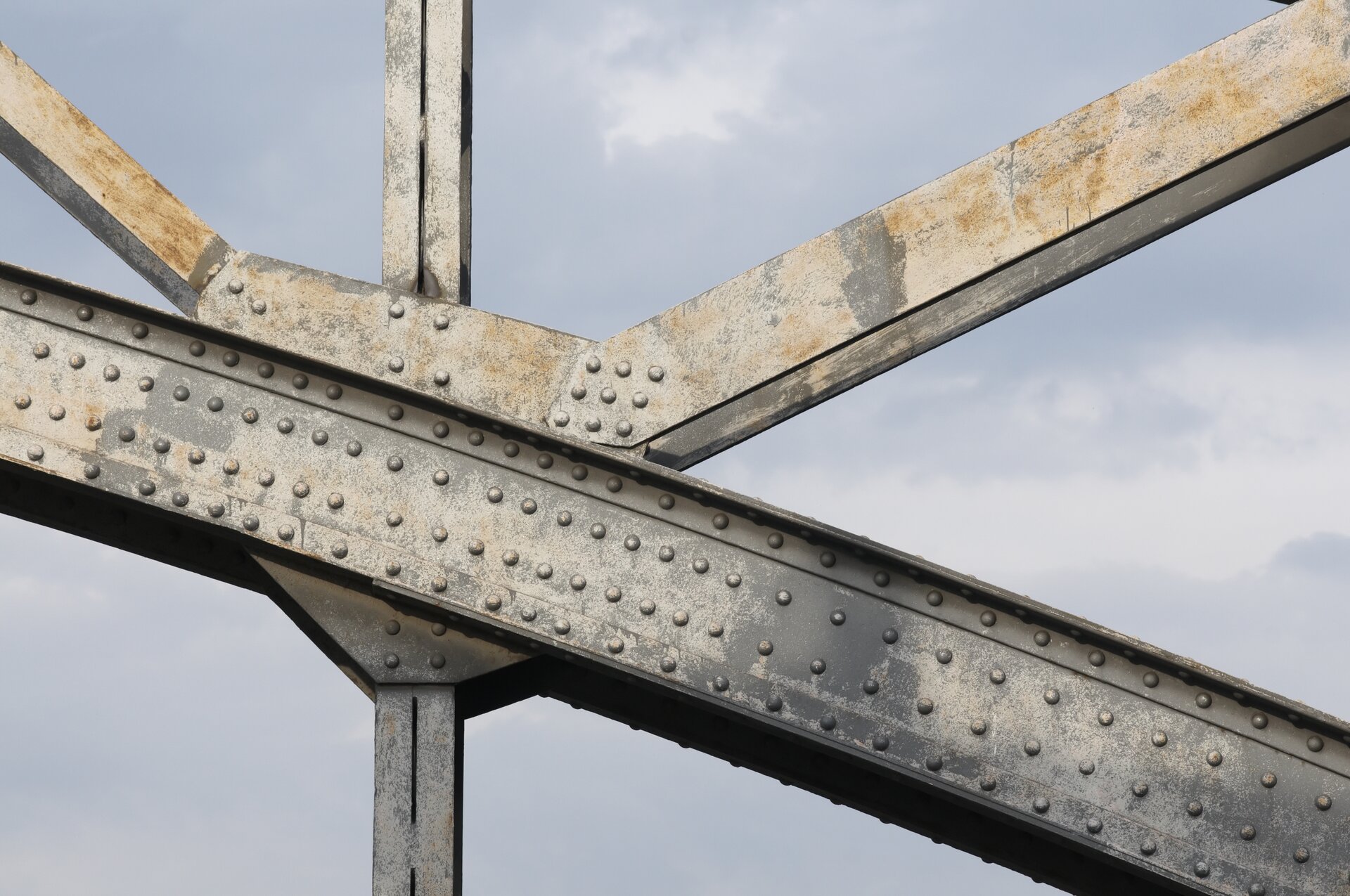 Zdjęcie przedstawia fragment konstrukcji nitowanej mostu stalowego. Widoczne są elementy stalowe połączone pod różnym kątem za pomocą nitów.