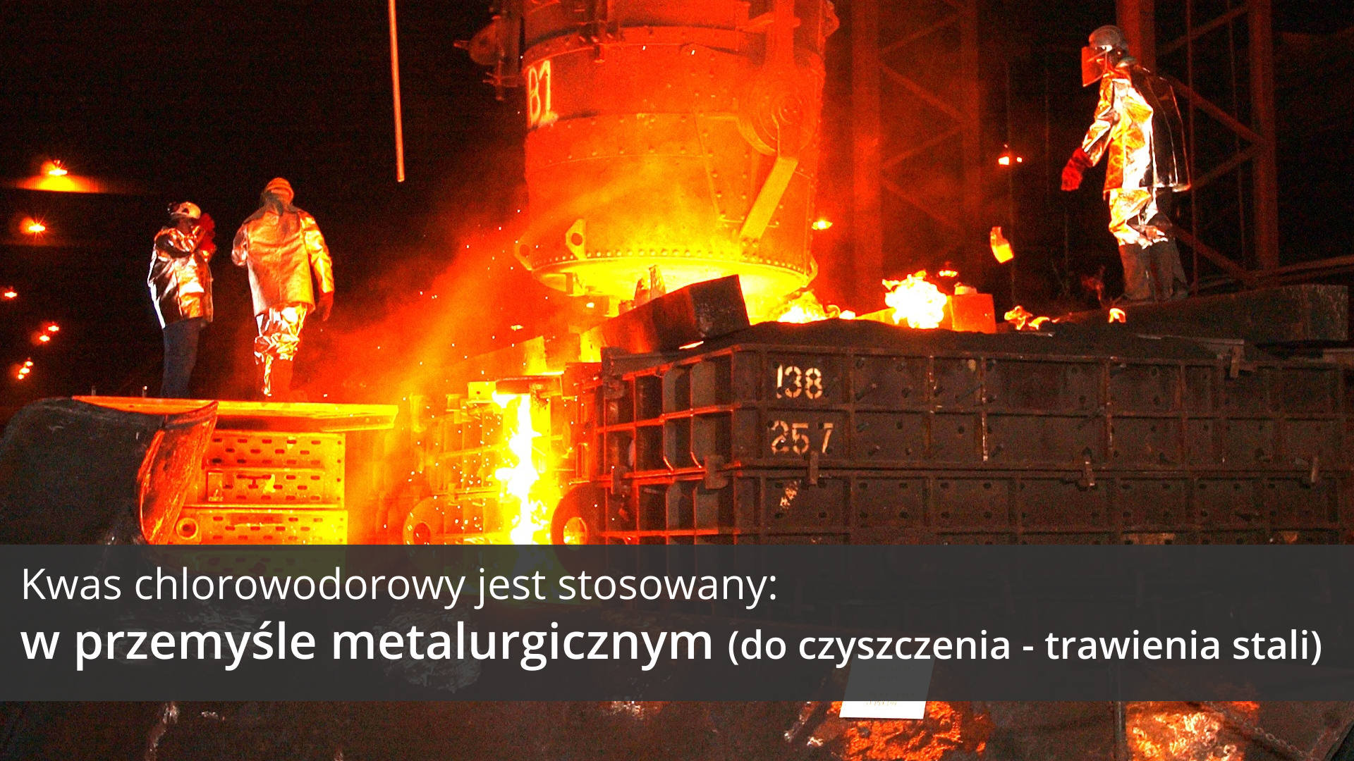 Druga ilustracja galerii przedstawia scenę wytopu stali w hucie stali. W pobliżu wylotu Wielkiego Pieca, z którego wylewa się rozjarzona do białości struga ciekłego metalu, stoi troje ludzi ubranych w kombinezony chroniące przed wysoką temperaturą. Różne elementy instalacji hutniczej oznaczone są rozmaitymi numerami. Na tle obrazka, w dolnej części ilustracji, znajduje się ciemnoszary pasek, na którym umieszczono jasny napis: Kwas chlorowodorowy jest stosowany w przemyśle metalurgicznym do czyszczenia, czyli trawienia stali.