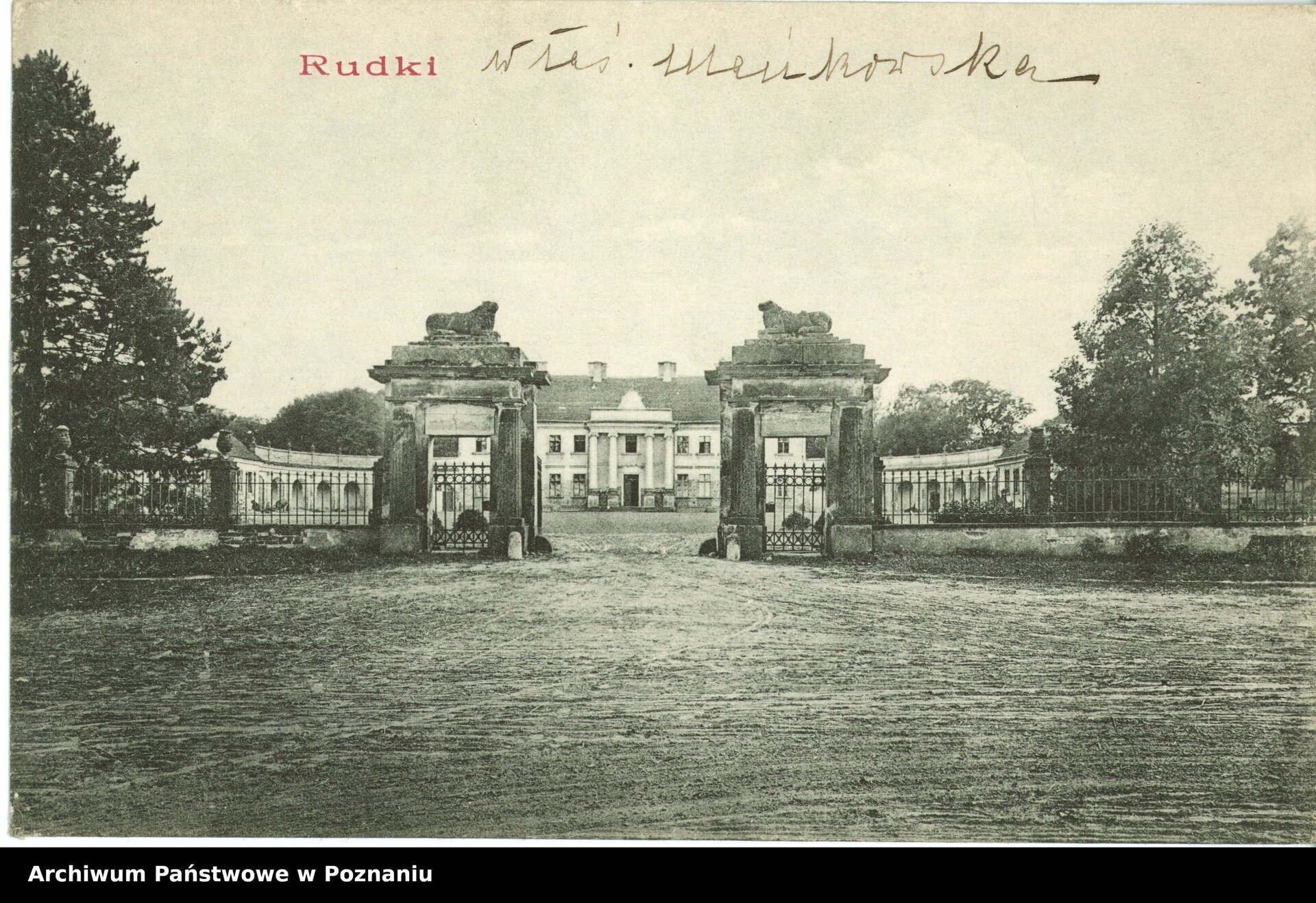 Zdjęcie z epoki przedstawiające pałac klasycystyczny z epoki Oświecenia w Rudkach. Na pierwszym planie okazała brama, obok niej dwie furty z kutego żelaza. Furty stoją między dwoma filarami, na szczycie których umieszczono rzeźbione figury lwów w dostojnych pozach leżących. Przed bramą i ogrodzeniem znajduje się rozległy plac. Na dalszym planie bryła pałacu z portykiem w Rudkach. Jasny budynek z okazałymi czterema kolumnami w portyku, skromną attyką na szczycie, częściowo zasłaniającą dwuspadowy dach. Zaokrąglone skrzydła gmachu budynku z kolumnadą częściowo zasłaniają drzewa, znajdujące się w części parkowej pałacu. Po obu stronach fotografii drzewa w linii ogrodzenia. Podpis u góry fotografii: “Rudki”, odręczny dopisek: “Wł. Mańkowska”