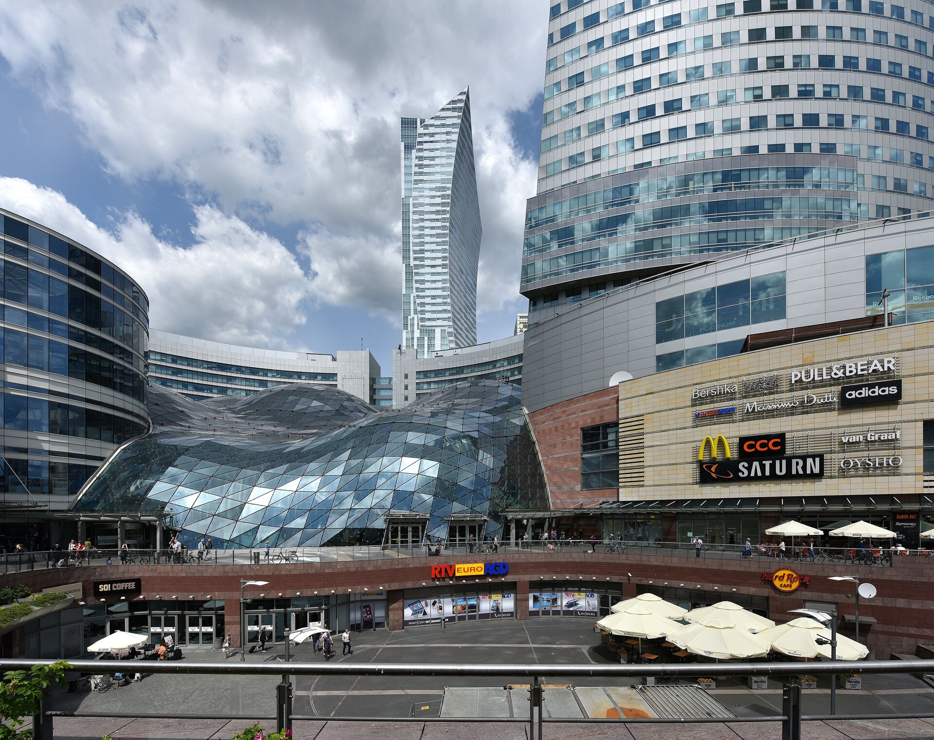 Ilustracja przedstawia Centrum Handlowe Złote Tarasy w Warszawie. Widzimy, że budynki centrum handlowego są całe oszklone i mają naturalne kształty jest to architektura blob, projektanta kalifornijskiej pracowni Jerde Partnership.