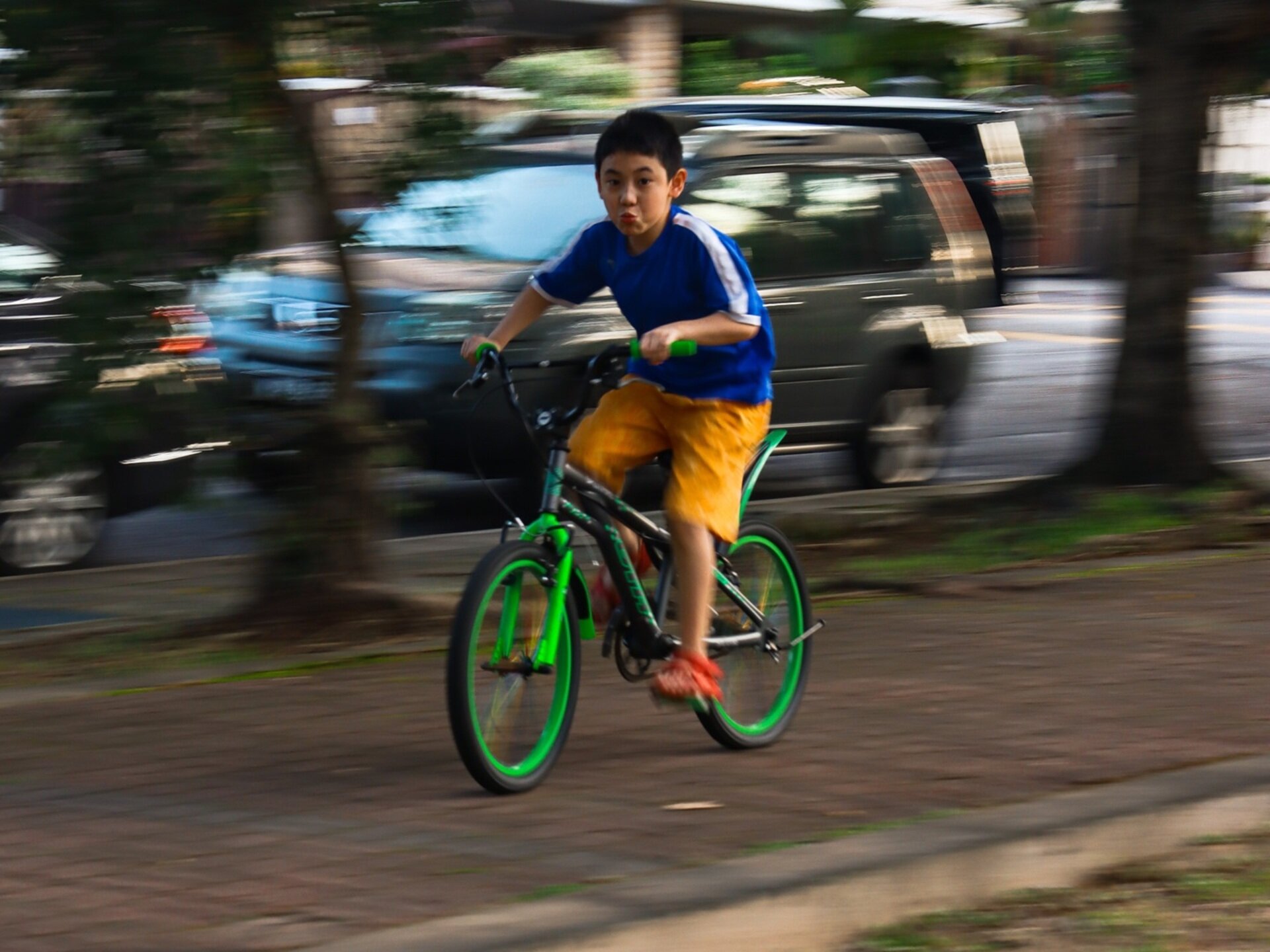 Zdjęcie przestawia chłopca w wieku szkolnym jadącego na rowerze.
