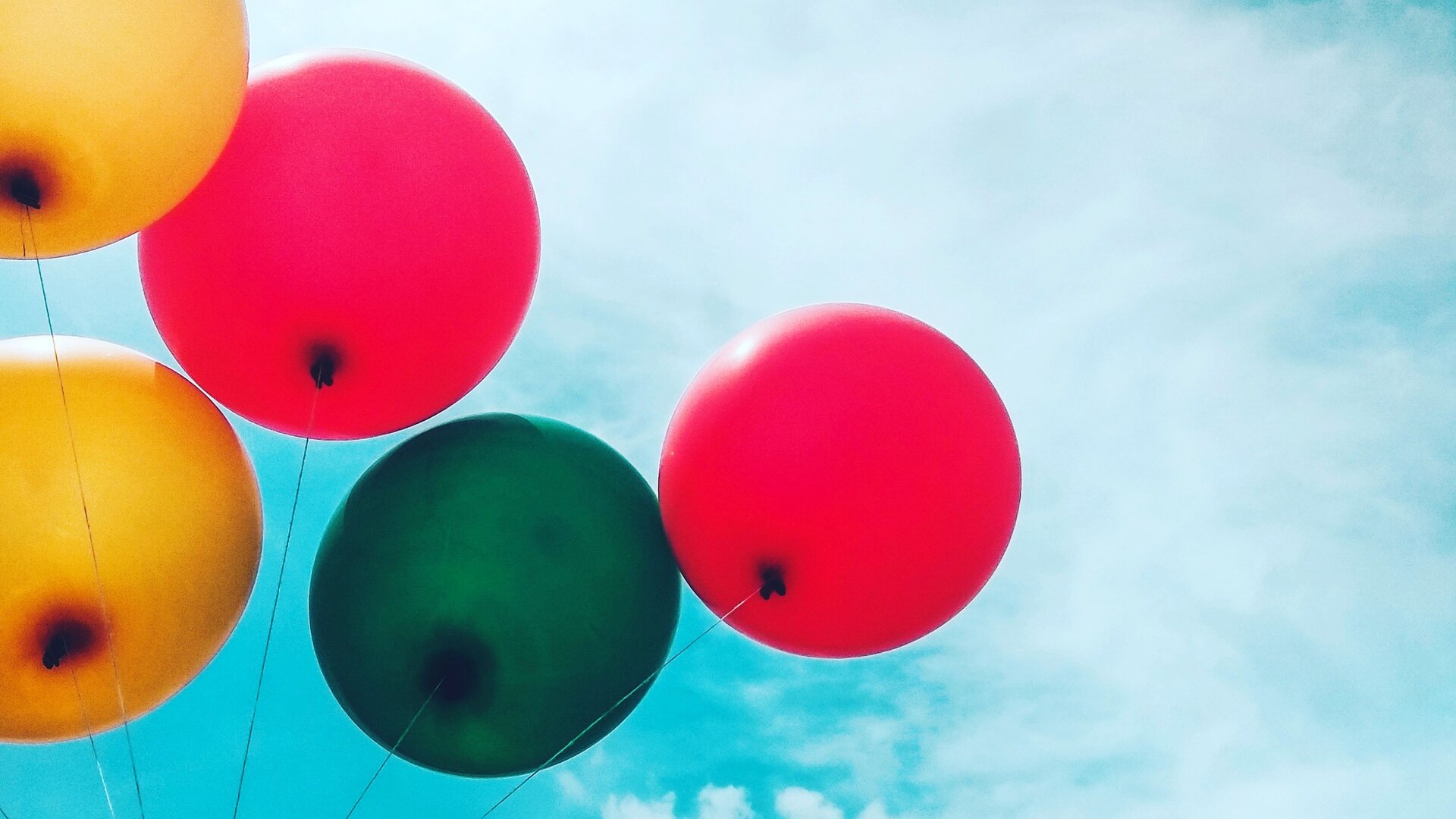 Zdjęcie poglądowe przedstawia kilka baloników uwiązanych na sznurkach na tle błękitnego pogodnego nieba. Balony są w kolorze czerwonym, zielonym i żółtym.