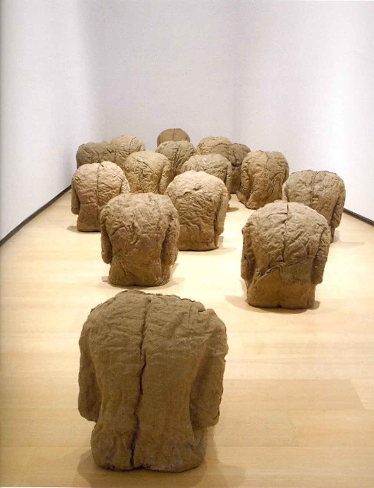 Magdalena Abakanowicz, „Plecy” Fotografia przedstawia rzeźbę umieszczoną w pomieszczeniu o jasnych ścianach oraz jasnych panelach, składającą się z piętnastu oddzielnych elementów. Każdy z nich swoim kształtem przypomina nieco zgarbione ludzkie plecy z fragmentem rąk. Z przodu fotografii umieszczono jedną część, następnie dwie, w bliższej odległości, a im dalej, tym bliżej siebie ustawione są kolejne elementy. Są one prawie identyczne, różnią się pofałdowaniem brązowoszarego materiału, przypominającego glinę.