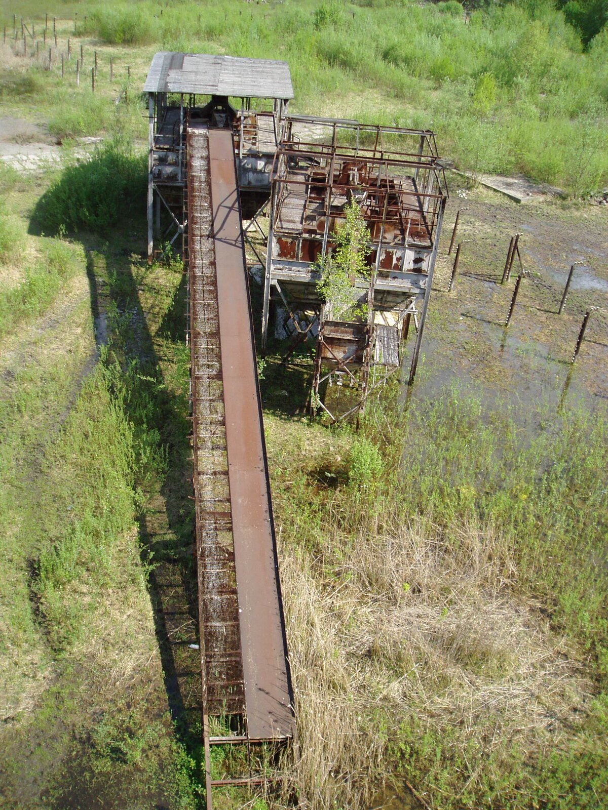 Ilustracja przedstawia część scenografii Allana Starskiego do filmu „Lista Schindlera” w reżyserii Stevena Spielberga w 1993 roku. Na fotografii znajdują się dwie szaro‑brązowe konstrukcje. Konstrukcja po lewej stronie, stoi dalej i  jest zadaszona. Jest do niej przystawiona długa, brązowa rampa. Obie konstrukcje są umiejscowione na podmokłym, zielonym terenie. Za nimi znajdują się 2 rzędy brązowych pachołków oraz zielona roślinność.