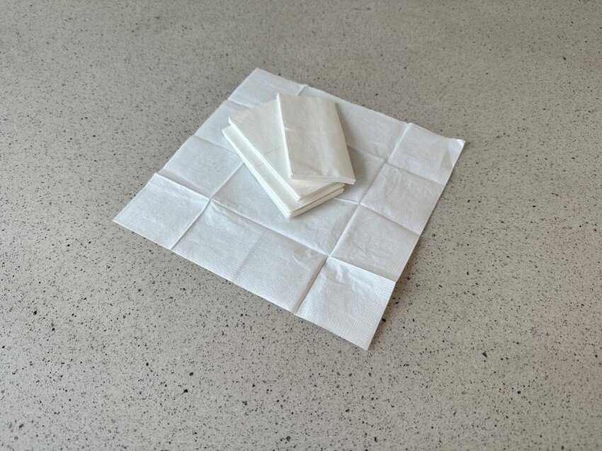 Zdjęcie przedstawia chusteczki higieniczne ułożone jedna na drugiej. Na samym spodzie stosu znajduje się rozłożona chusteczka.