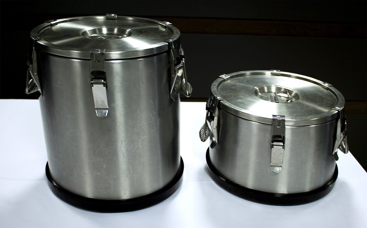 Na zdjęciu znajdują się dwa srebrne termosy do cateringowego transportu potraw. Lewy termos jest dwa razy wyższy od prawego.