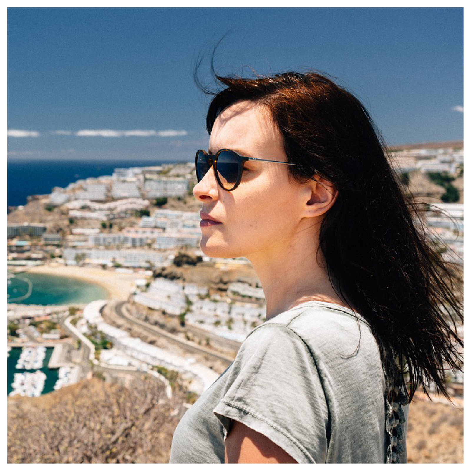 Ilustracja przedstawia kobietę stojącą na wzniesieniu na tle nadmorskiego miasta.