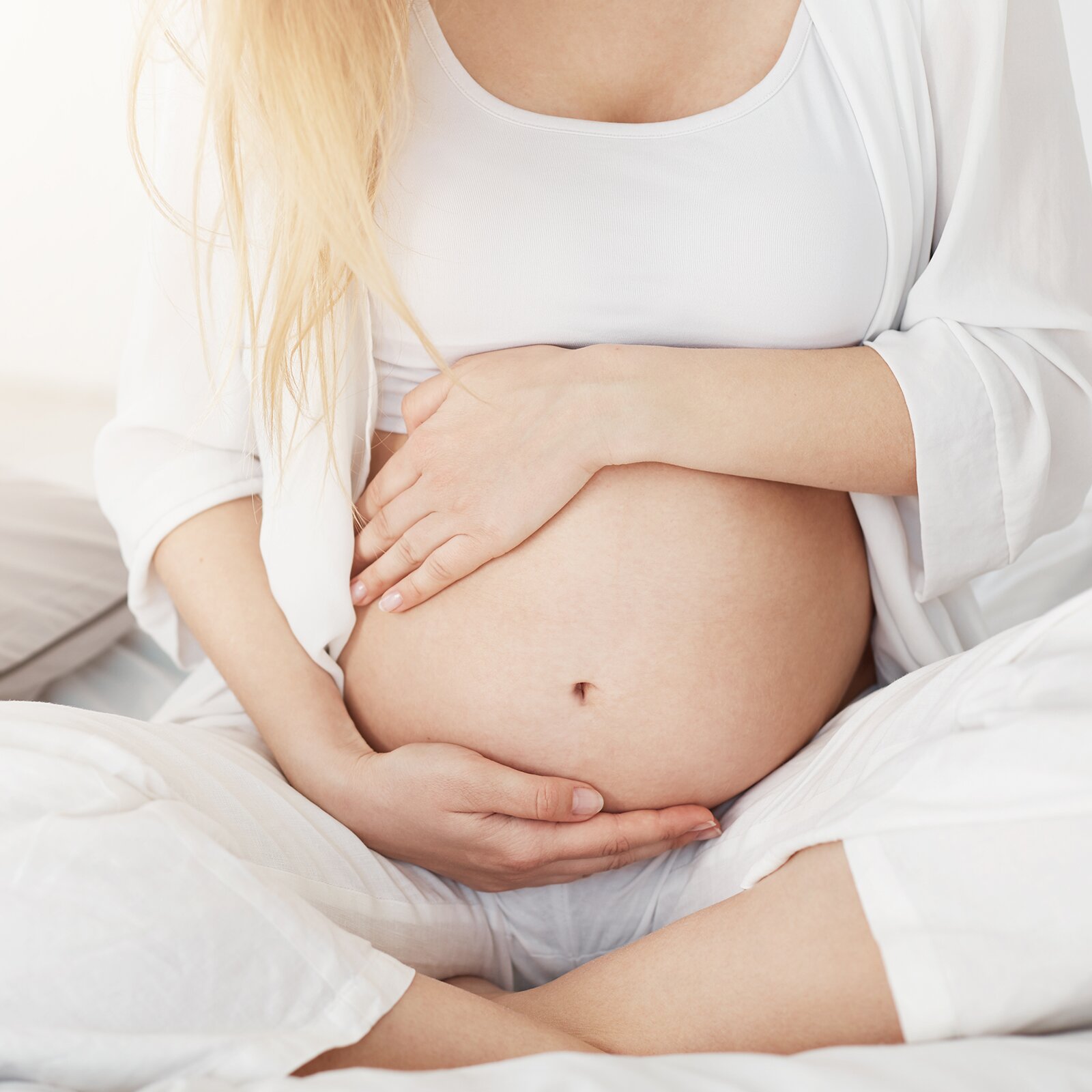 Zdjęcie przedstawia ciężarną kobietę, która obejmuje dłońmi swój brzuch. 