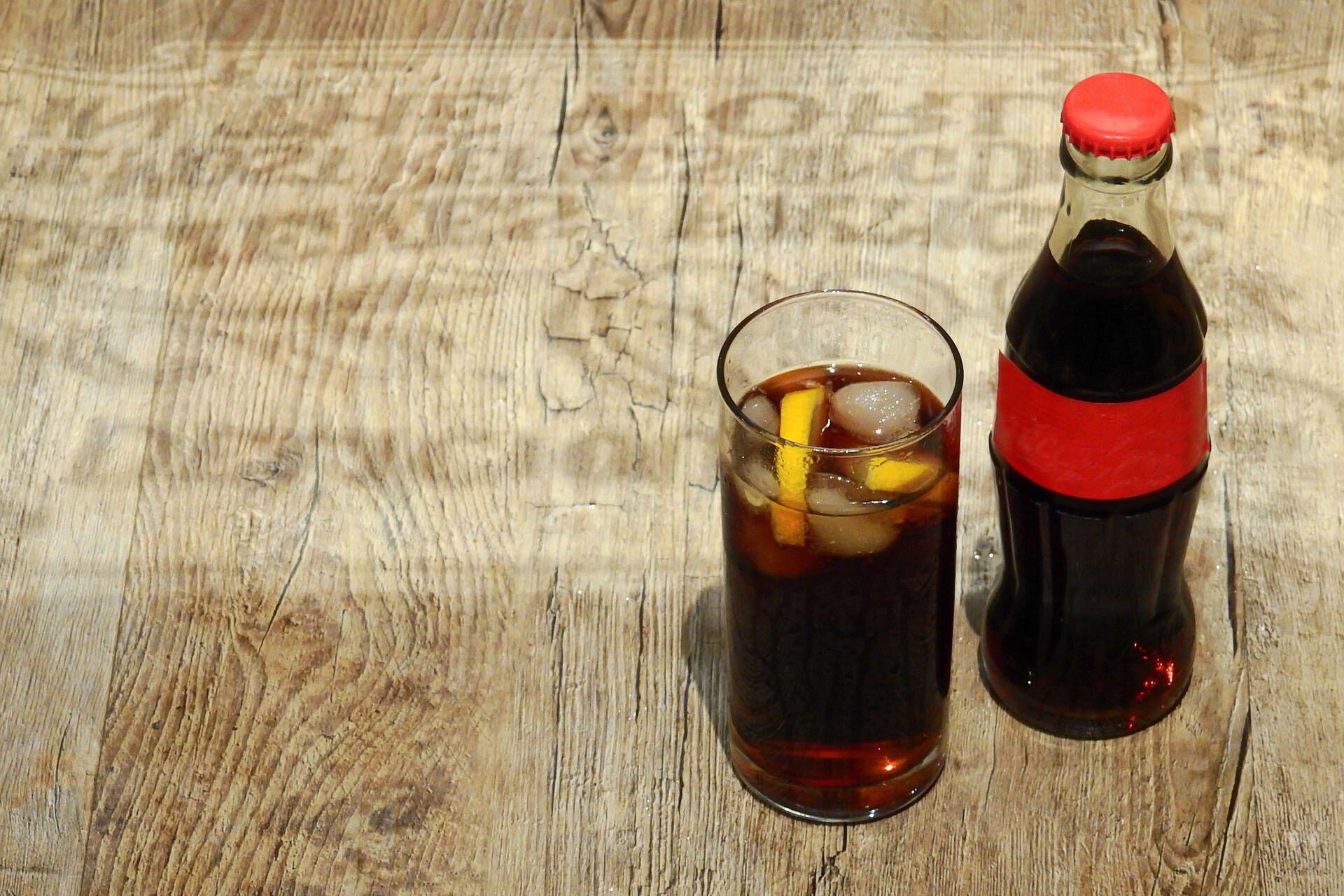 Zdjęcie przedstawia szklankę i butelkę coli.