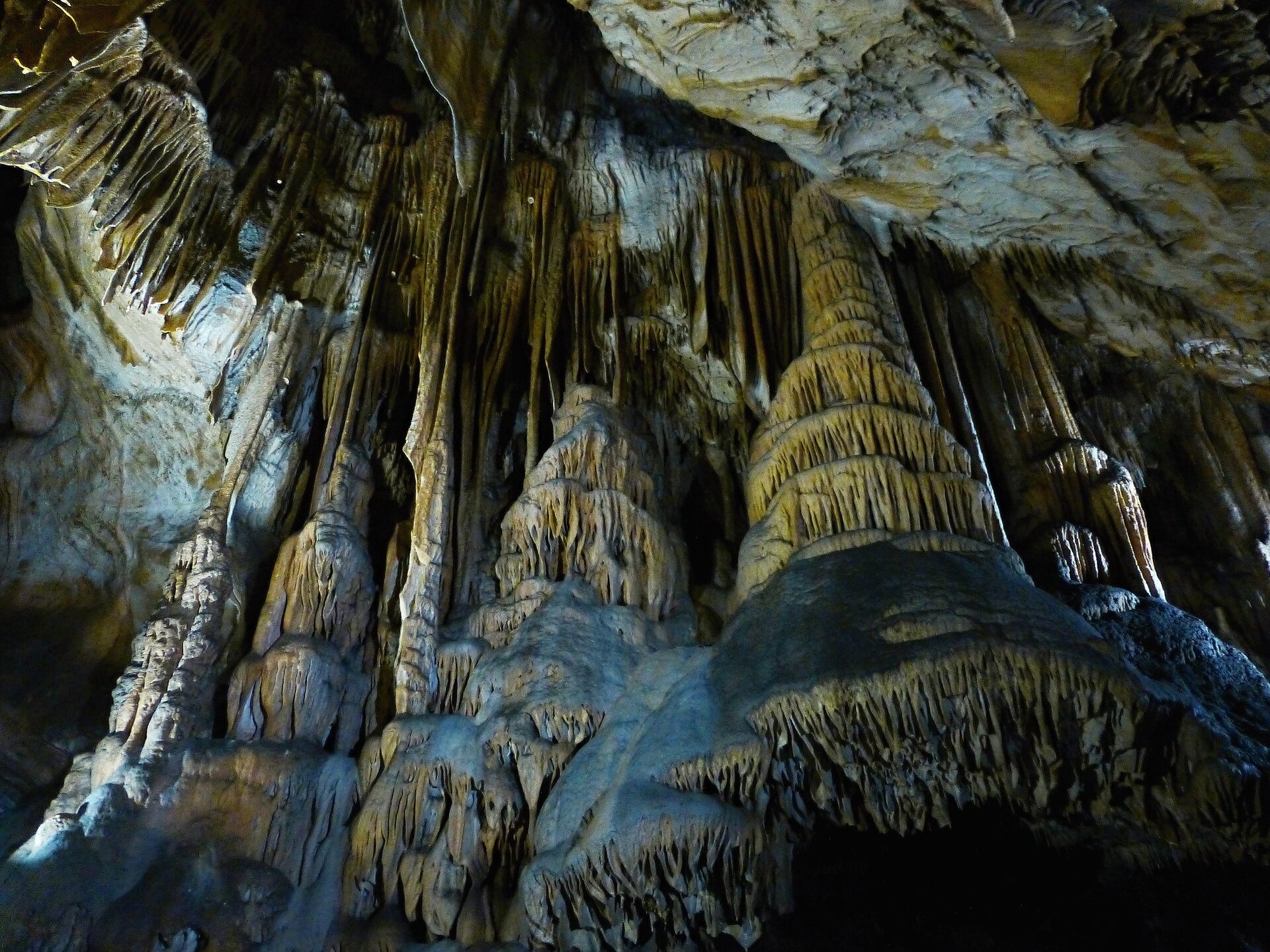  Na zdjęciu wnętrze jaskini. Widoczne są formy naciekowe stalaktyty, stalagmity i stalagnaty. Formy mają biało‑żółty kolor. 