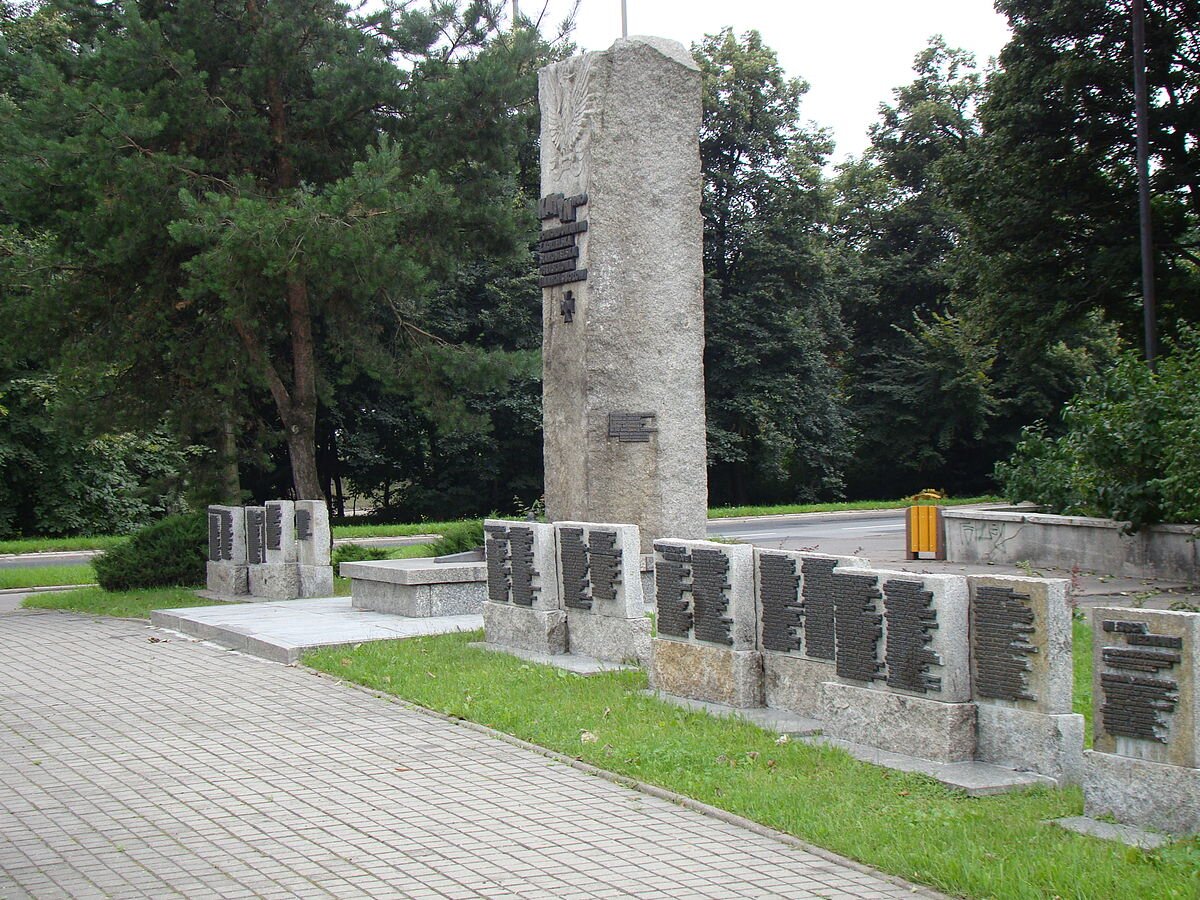 Ilustracja przedstawia pomnik. Na monumencie, mającym postać czworobocznego słupa wykonanego z granitu, znajduje się godło Polski i napis: Katyń 1940. Pomordowanym z Kozielska, Ostaszkowa, Starobielska i innych obozów. Obok niewielkie płyty z nazwiskami poległych.