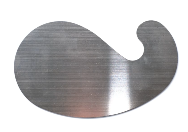 Zdjęcie przedstawia cyklinę. Jest to płaskie narzędzie w metalicznym kolorze. Ma obły kształt.