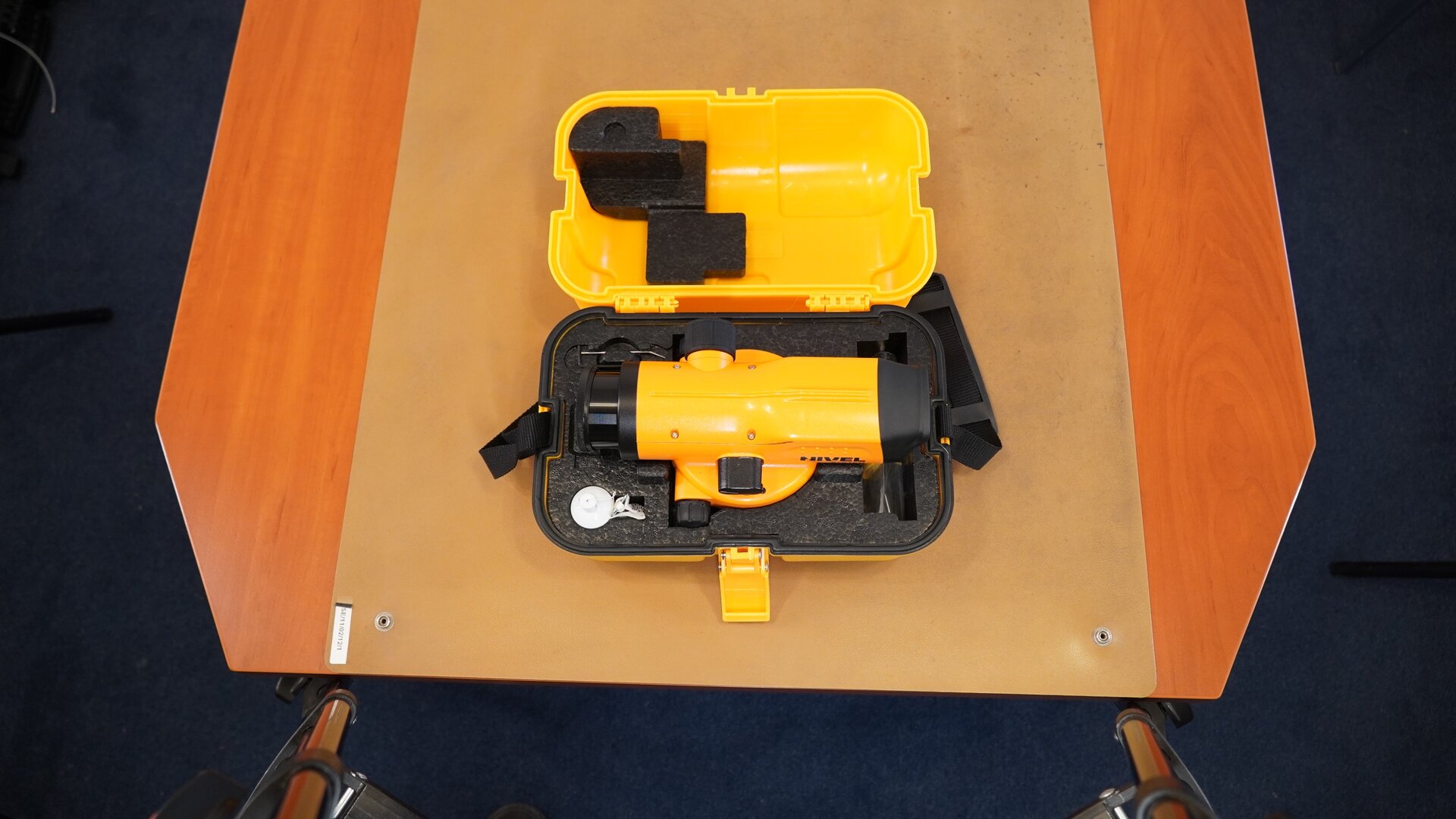 Zdjęcie ukazuje tę samą skrzynkę, która została przedstawiona na poprzedniej fotografii, po otwarciu. W środku znajduje się podłużne urządzenie pomiarowe, czyli niwelator. Instrument  został zabezpieczony styropianowym wypełnieniem chroniącym przed uszkodzeniem.