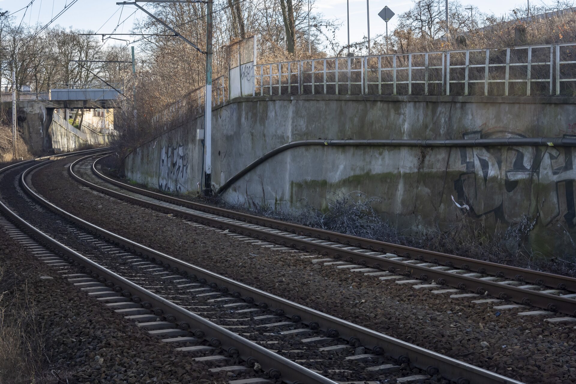  Na zdjęciu widać mur oporowy, który biegnie wzdłuż torowiska. Mur został wykonany z żelbetonu. Na ujęciu widoczne są instalacje przymocowane do jednej ze ścian muru oporowego.