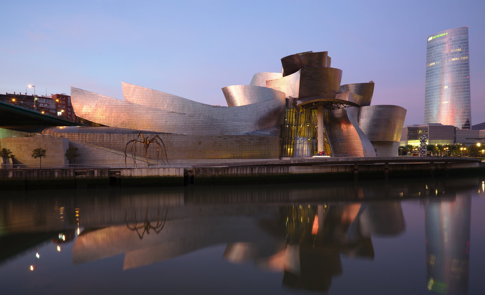 Ilustracja interaktywna przedstawia widok na budynek położony nad rzeką widoczną przed nim, na tle ciemniejącego nieba oraz innych budynków. Budynek wyglądem przypomina łódź. Ściana z wejściem do budynku po prawej stronie jest przeszkolona, a samo wejście podświetlone jest na zewnątrz w kolorze żółtym. Przed nim widać gruby, kremowy filar. Podtrzymuje on konstrukcję wysuniętego dachu, którego fragmenty przypominają srebrne kadłuby łodzi. Ściany również pozbawione są kątów prostych, a ich kształt także przywodzi na myśl długie łodzie. Przed budynkiem widoczny jest brukowany plac, na którym po lewej stronie umieszczono rzeźbę – dużego pająka na cienkich, wysokich nogach. 