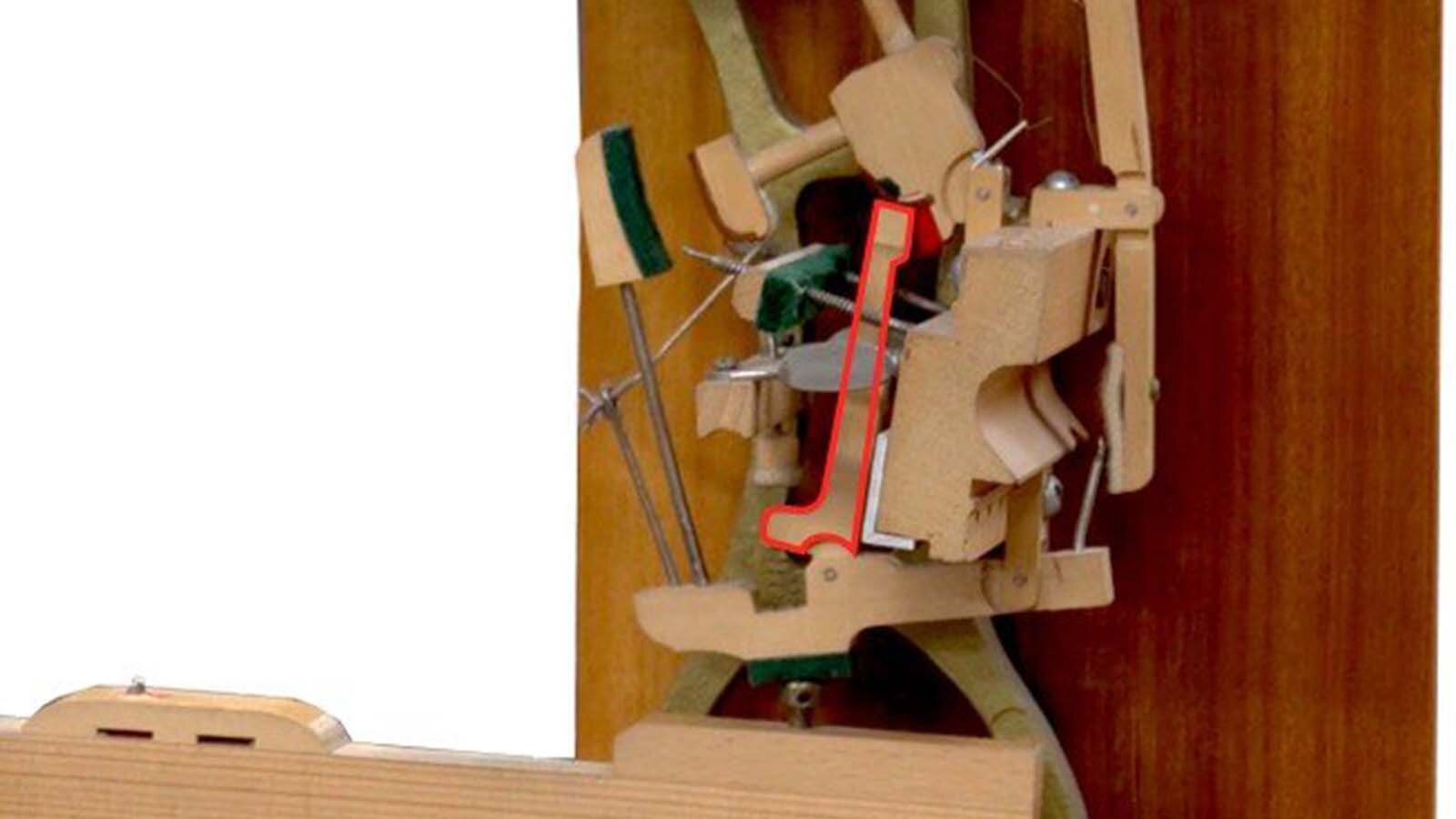 Zdjęcie przedstawia podzespół mechanizmu pianinowego lub fortepianowego jakim jest popychacz. Element został zaznaczony czerwoną obwódką.