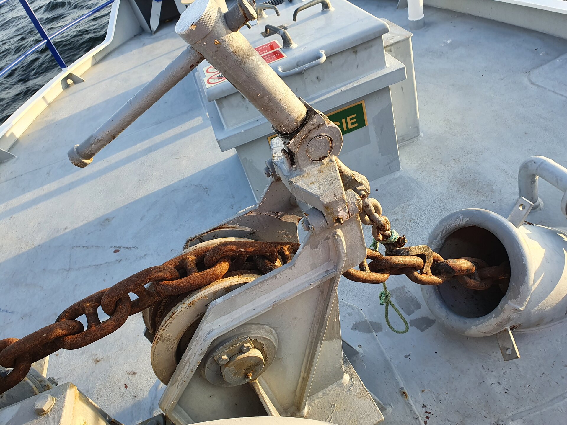 Zdjęcie przedstawia stoper zapadkowy. Widoczny jest łańcuch umieszczony w mechanizmie stopera. Łańcuch za stoperem znika w kluzie kotwicznej.