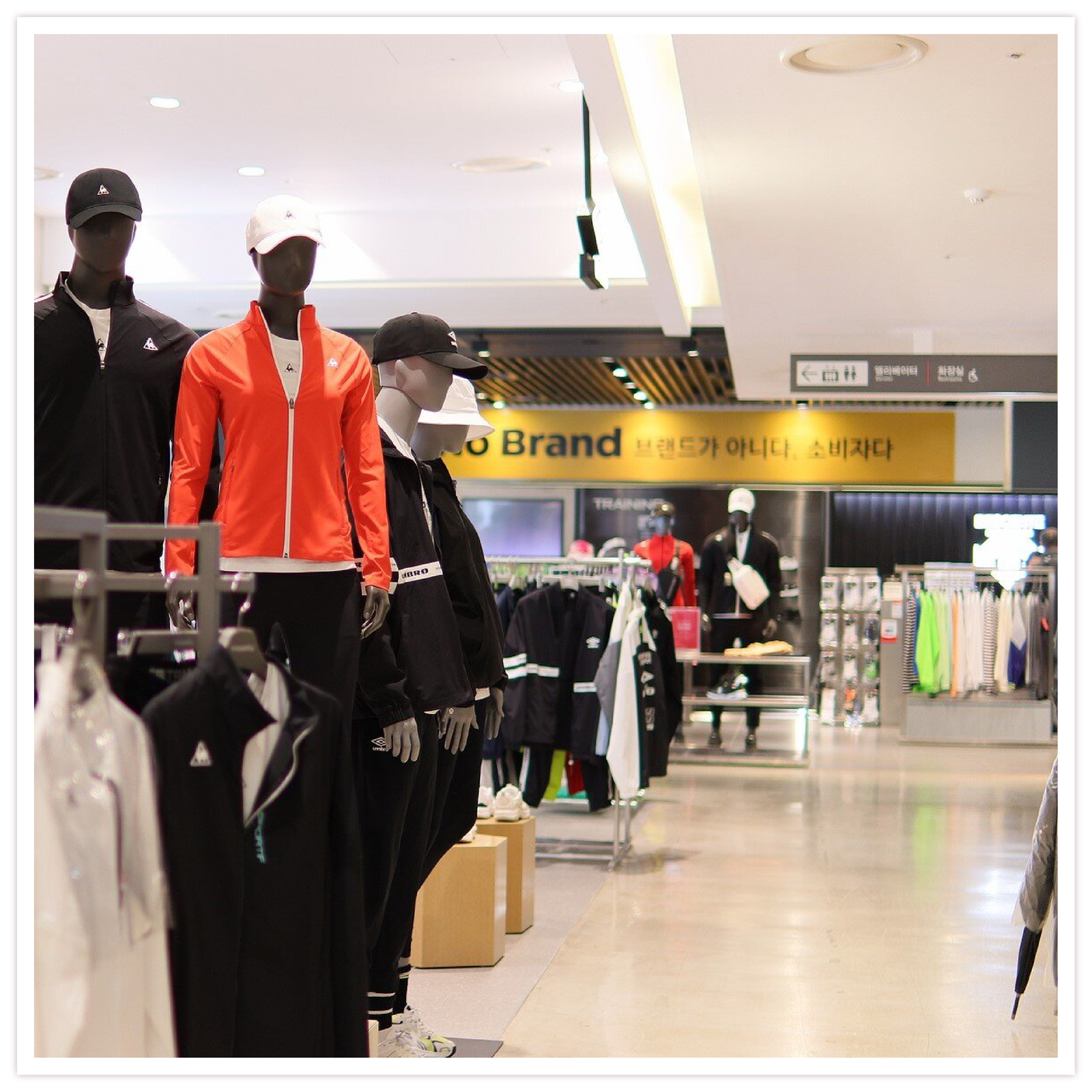 Na zdjęciu widoczne jest wnętrze sklepu sportowego w galerii handlowej. Ubrania wiszą na wieszakach. Na środku sklepu stoją cztery manekiny ubrane w czapki z daszkiem, bluzy, koszulki, dresy i sportowe buty. 