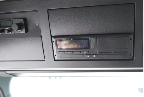 Zdjęcie przedstawia tachograf. Jest to urządzenie umieszczone w podsufitce samochodu. Widoczny jest ekran oraz przyciski umożliwiające wykonanie wydruku.