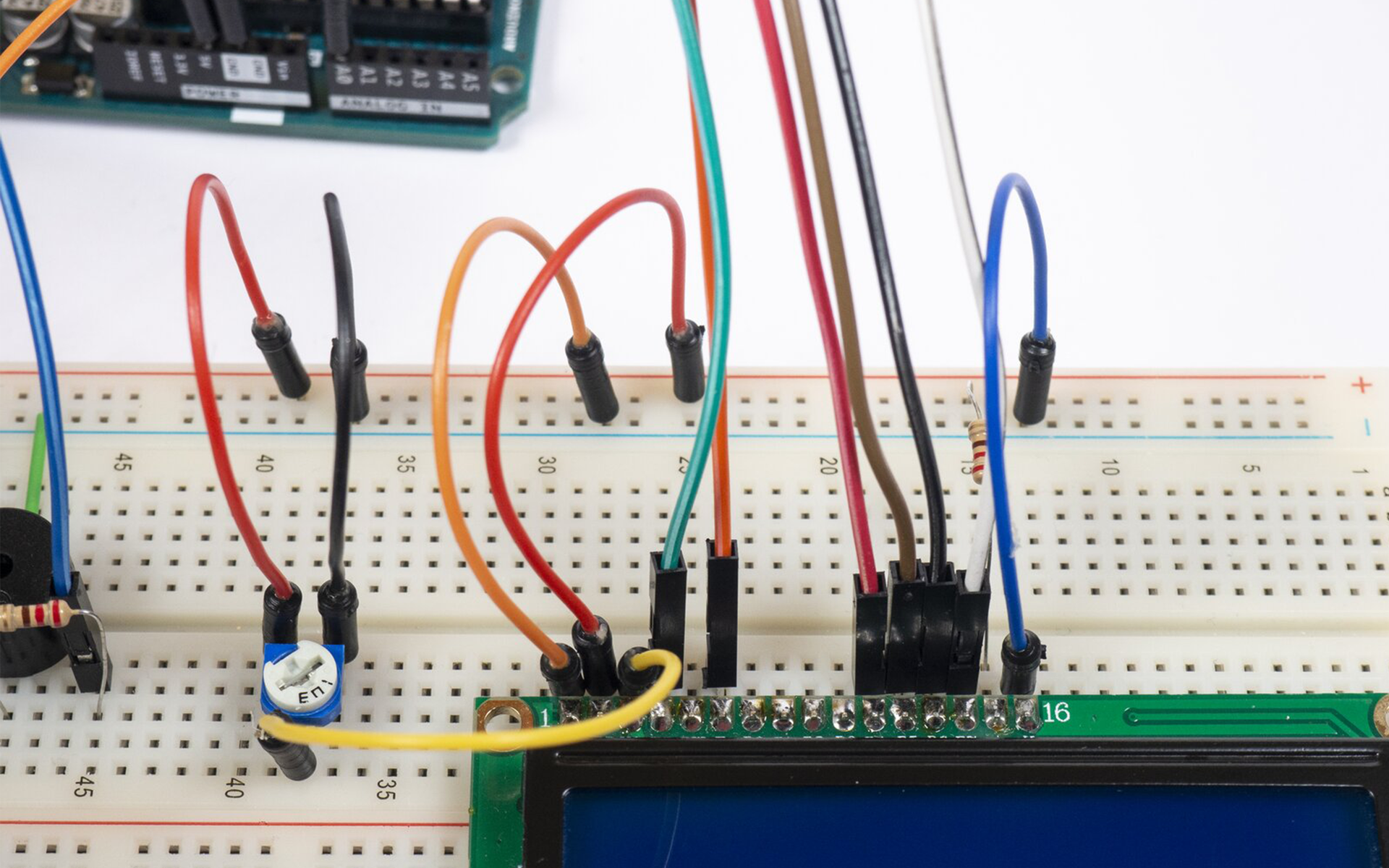 Zdjęcie przedstawia połączenia pomiędzy arduino uno, a płytką stykową. Na płytce znajduje się termometr (względem wycięcia w obudowie) podłączony jest prawą nóżką do uziemienia, lewą do +5V a środkową do pinu A0 arduino. Pin 5V podłączony jest do +5V płytki, a GND podłączone jest do uziemienia. Uziemienie górnej szyny jak i dolnej na płytce stykowej jest połączone. Podłączona jest także LED, jedną nóżką do uziemienia, drugą zaś poprzez rezystor do pinu 7 arduino. Po środku płytki zamontowany jest brzęczyk, który poprzez rezystor łączy się z pinem 6 arduino, a drugą nóżką do uziemienia. Po prawej stronie płytki stykowej podłączono ekran LCD, do którego podłączono kable prowadzące do arduino. Pomiędzy ekranem a brzęczykiem zamontowano potencjometr, do jego nóżek podłączono kable, środkowy do 3 pinu ekranu, lewa nóżka do +5V natomiast prawy do uziemienia. Ostatni i pierwszy pin ekranu podłączono do uziemienia płytki, przedostatni pin podłączono rezystorem do węzła dodatniego płytki. Do 2 pinu ekranu dołączono kabel z węzła dodatniego płytki.