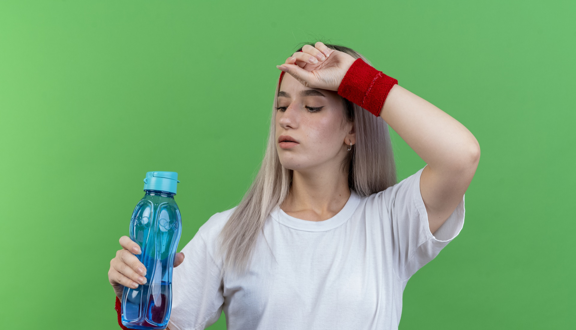 Zdjęcie przedstawia nastolatkę, która trzyma w prawej dłoni bidon z wodą. Lewą dłoń opiera o czoło. 