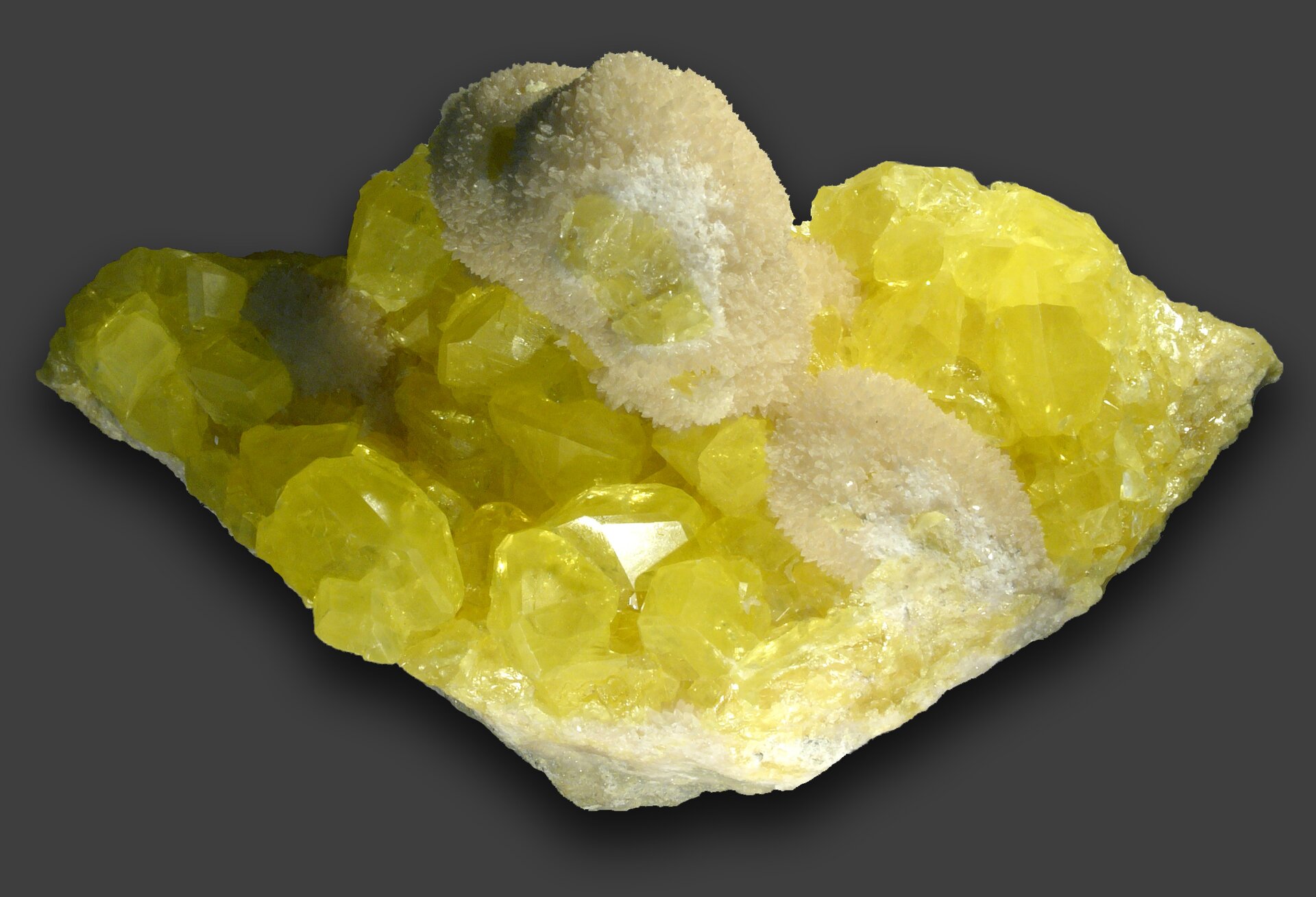 Zdjęcie przedstawia odłamek żółtej siarki składający się z większych i mniejszych kryształów.