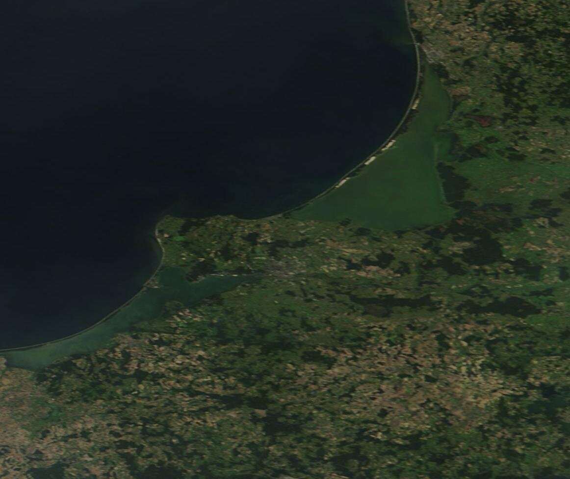 Zdjęcie satelitarne przedstawia fragment wybrzeża. Linia brzegowa przebiega łukowato. Po lewej stronie zdjęcia ląd wybrzusza się w stronę morza.