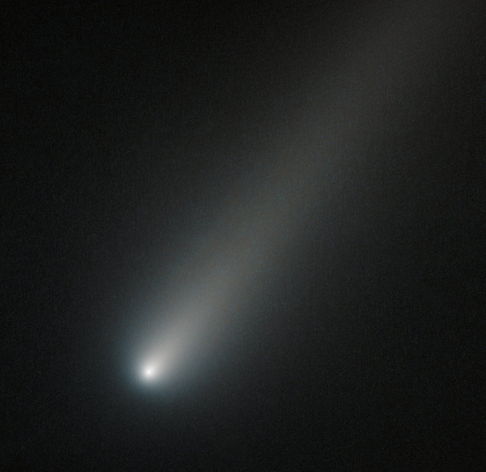 Zdjęcie przedstawia kometę ISON uwiecznioną przez teleskop Hubble'a podczas przelotu przez orbitę Marsa podczas zbliżenia do Układu Słonecznego w 2013 roku na miesiąc przed osiągnięciem peryhelium. Kometa zajmuje praktycznie cały kadr, jej jądro świeci jasnym światłem, a ogon jest wyraźny.
