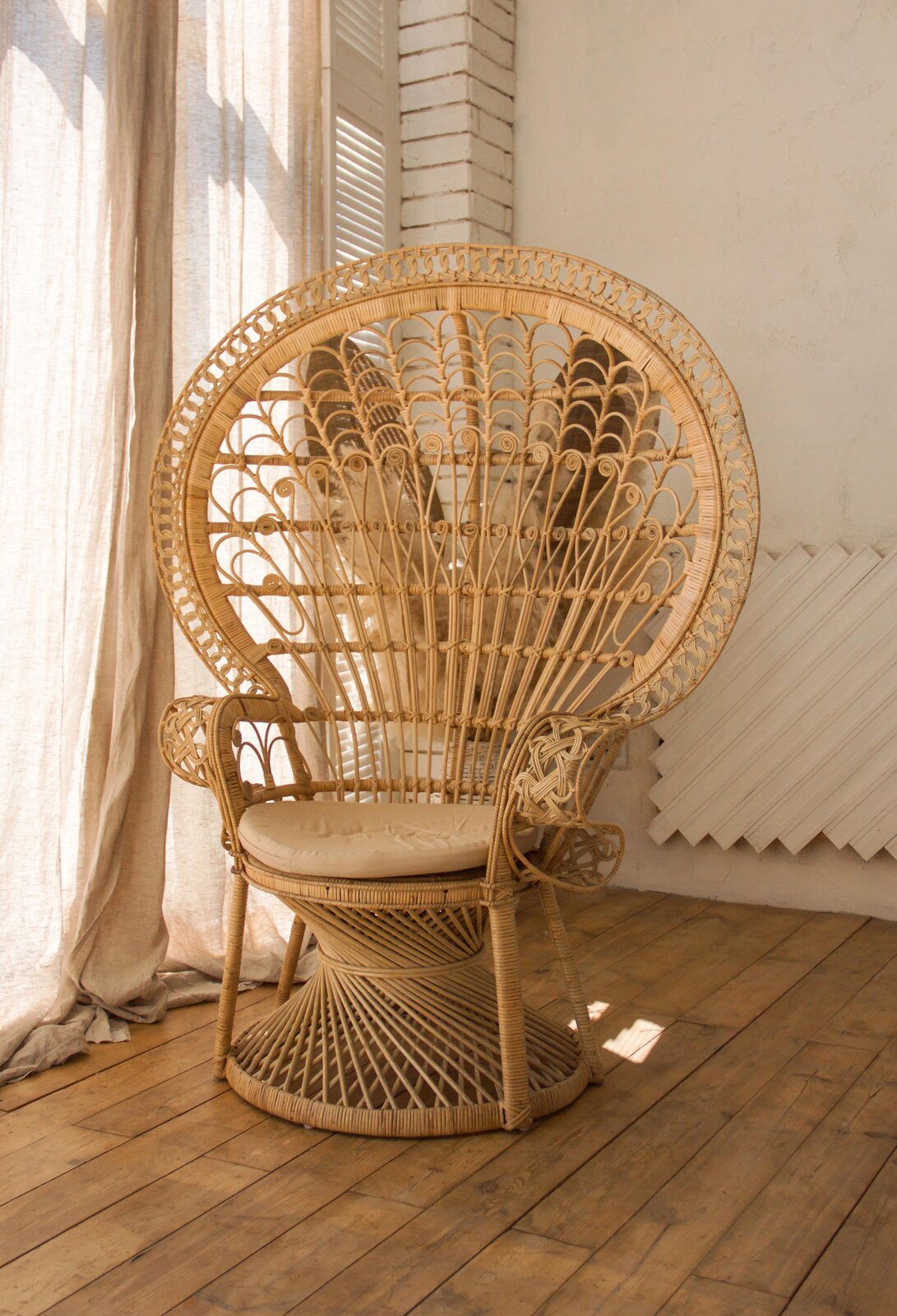 Zdjęcie fotela wiklinowego w jasnym kolorze z ozdobnym półokrągłym oparciem. Siedzisko fotela jest okrągłe.