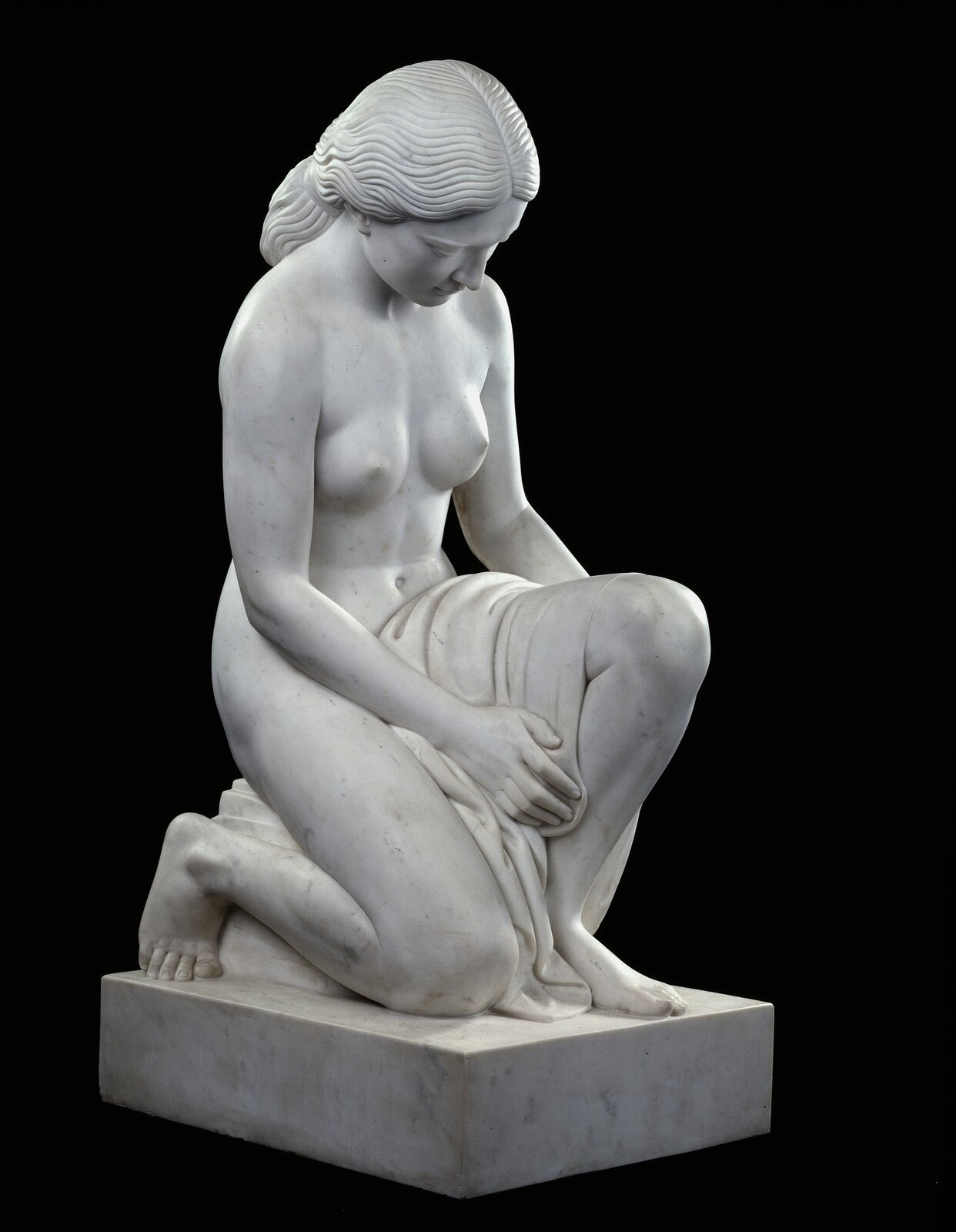 Zdjęcie przedstawia pomnik autorstwa Paula Manship, pod tytułem: „Susanna”.  Rzeźba przedstawia klęcząca kobietę. Kobieta jest naga. Na jej lewej nodze znajduje się zwinięty materiał. Kobieta ma pochyloną głowę, jej wzrok skierowany jest w dół. Włosy kobiety uczesane są w kitkę. Rzeźba jest koloru białego. Tło jest koloru czarnego. 