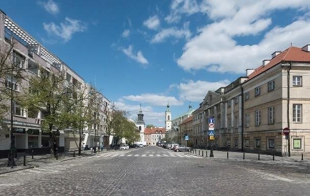 Nowoczesny budynek (po lewej) sąsiadujący z zabytkową zabudową Starego Miasta  (po prawej). Między nimi znajduje się brukowana ulica. 