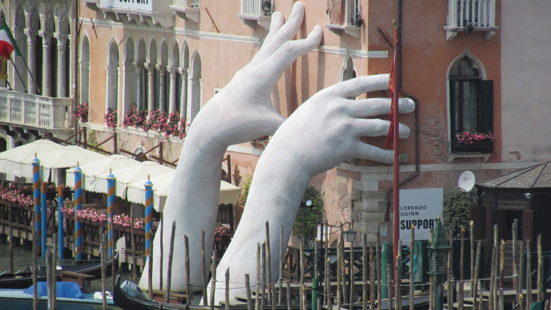 Zdjęcie przedstawia parę gigantycznych rąk wynurzających się z kanału w Wenecji. Podtrzymują one ściany jednej z zabytkowych, weneckich kamienic. Ręce wydają się powstrzymywać czternastowieczny  budynek od wpadnięcia do wody. Na dłoniach widoczne są zmarszczki i paznokcie. Instalacja artystyczna  została przygotowana przez włoskiego artystę  Lorenzo Quinn podczas międzynarodowego festiwalu sztuki w Wenecji Biennale di Venezia w 2017 roku. 