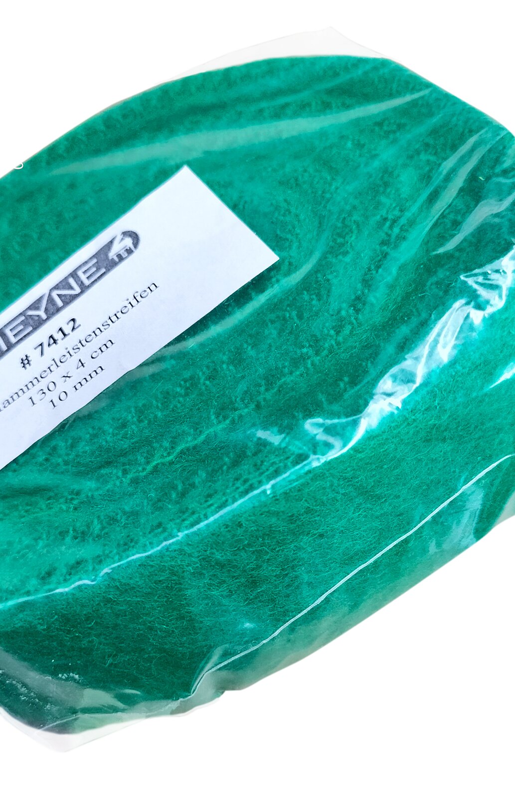 Zdjęcie przedstawia filc tkany. Widoczny jest zwój zielonego filcu w ujęciu z ukosa, w przeźroczystym foliowym opakowaniu z białą etykietą pośrodku, z czarnymi napisami.