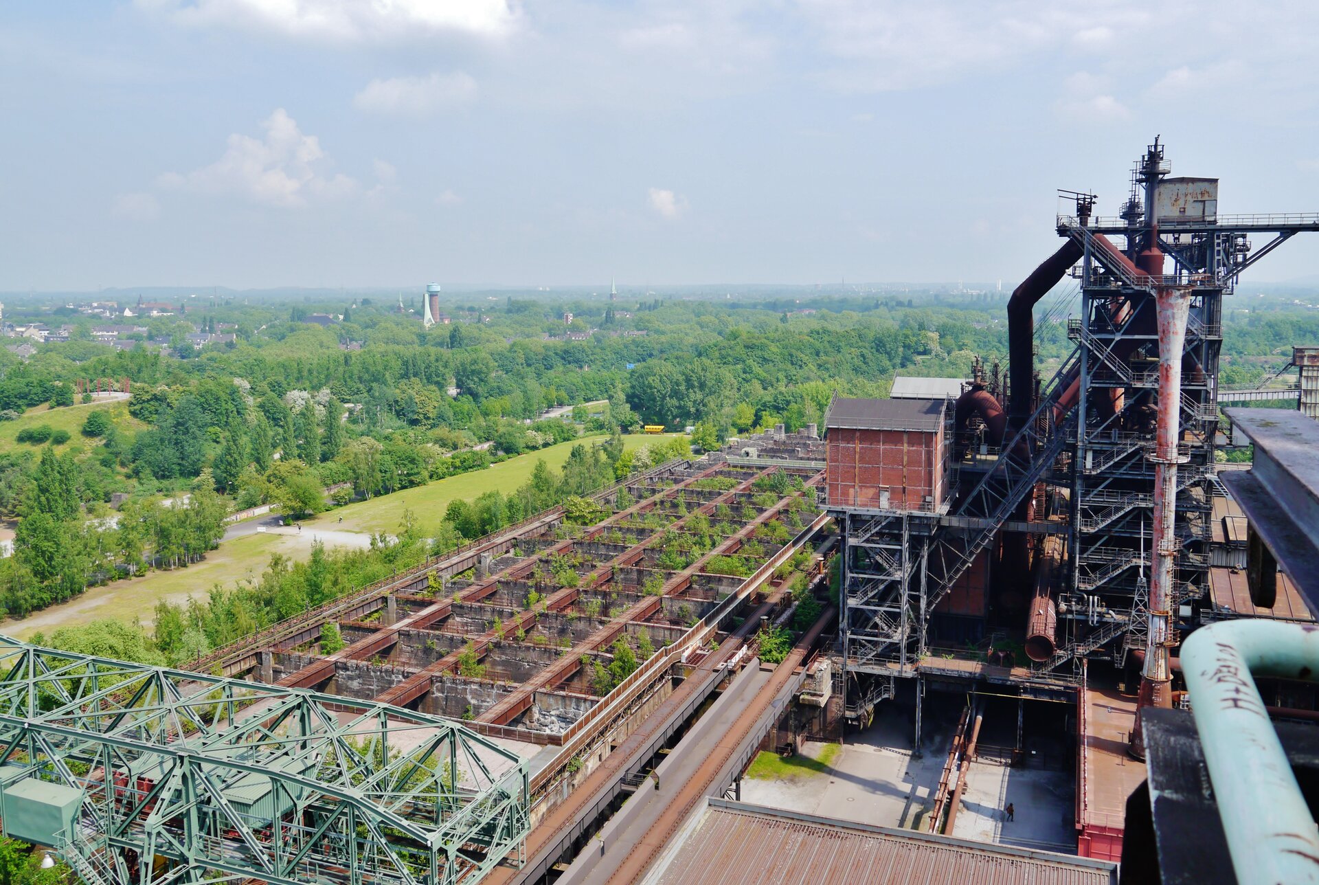 Zdjęcie wykonane ze szczytu metalowej konstrukcji dawnych zabudowań kopalni. Na drugim planie płaski teren porośnięty lasem.
