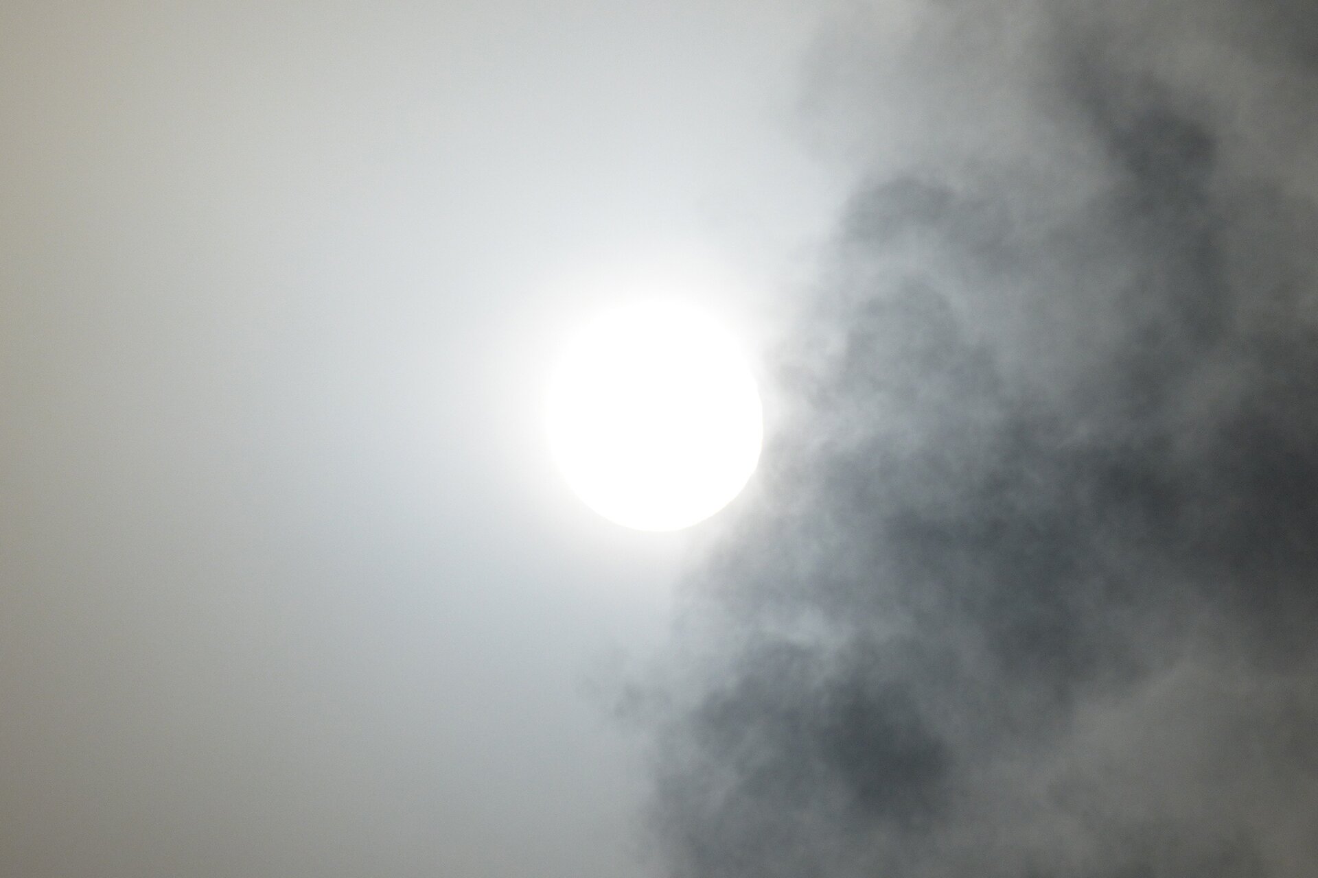 Fotografia przedstawia słońce. Po prawej stronie jest lekko przysłonięte przez ciemny obłok. Prawa strona mocno oświetlona, zlewa się z okręgiem słońca.