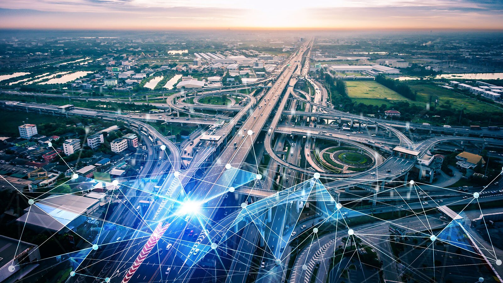 Zdjęcie z lotu ptaka, lekko z ukosa, przedstawia sieć krzyżujących się dróg oraz zjazdów i wjazdów na autostradę. Pomiędzy wiaduktami i ślimakami sieci drogowej widoczne są budynki, zaś w tle pasy zieleni, budynki, a na horyzoncie wschód słońca. Na drogami, nałożona na zdjęcie, widoczna sieć połączeń elektrostatycznych w postaci punktów połączonych liniami w łączące się trójkąty.