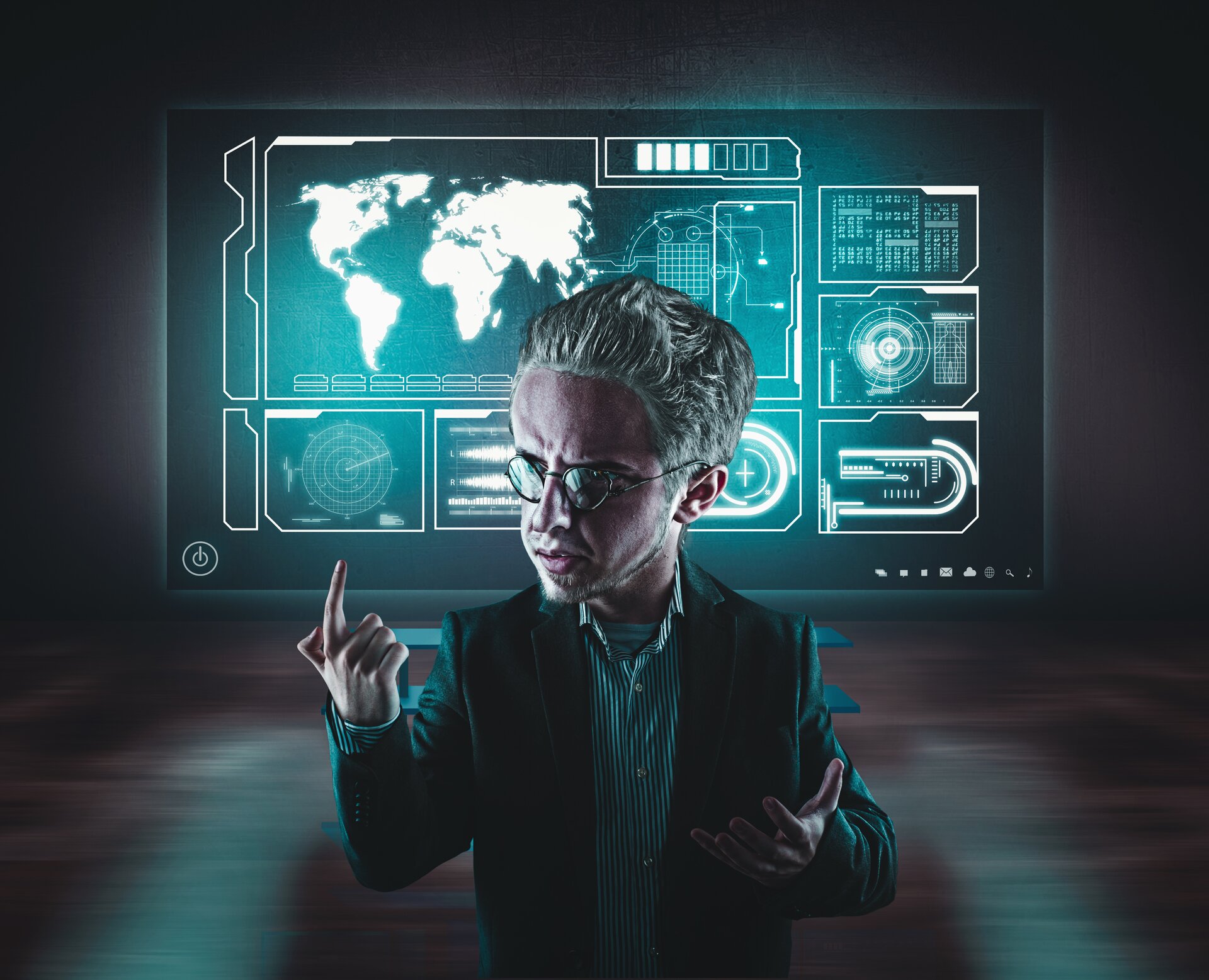 Ilustracja przedstawia mężczyznę. Zdjęcie zostało wykonane w taki sposób, że postać wygląda karykaturalnie. Głowa jest nieproporcjonalna do pozostałych części ciała - dużo większa. Mężczyzna ma okulary, ubrany jest w koszulę oraz marynarkę. Prawą rękę ma zgiętą w łokciu, a palec wskazujący jest skierowany w górę. Za nim znajduje się podświetlona tablica, na której wyświetla się mapa i różne elementy pomocnicze do mapy.