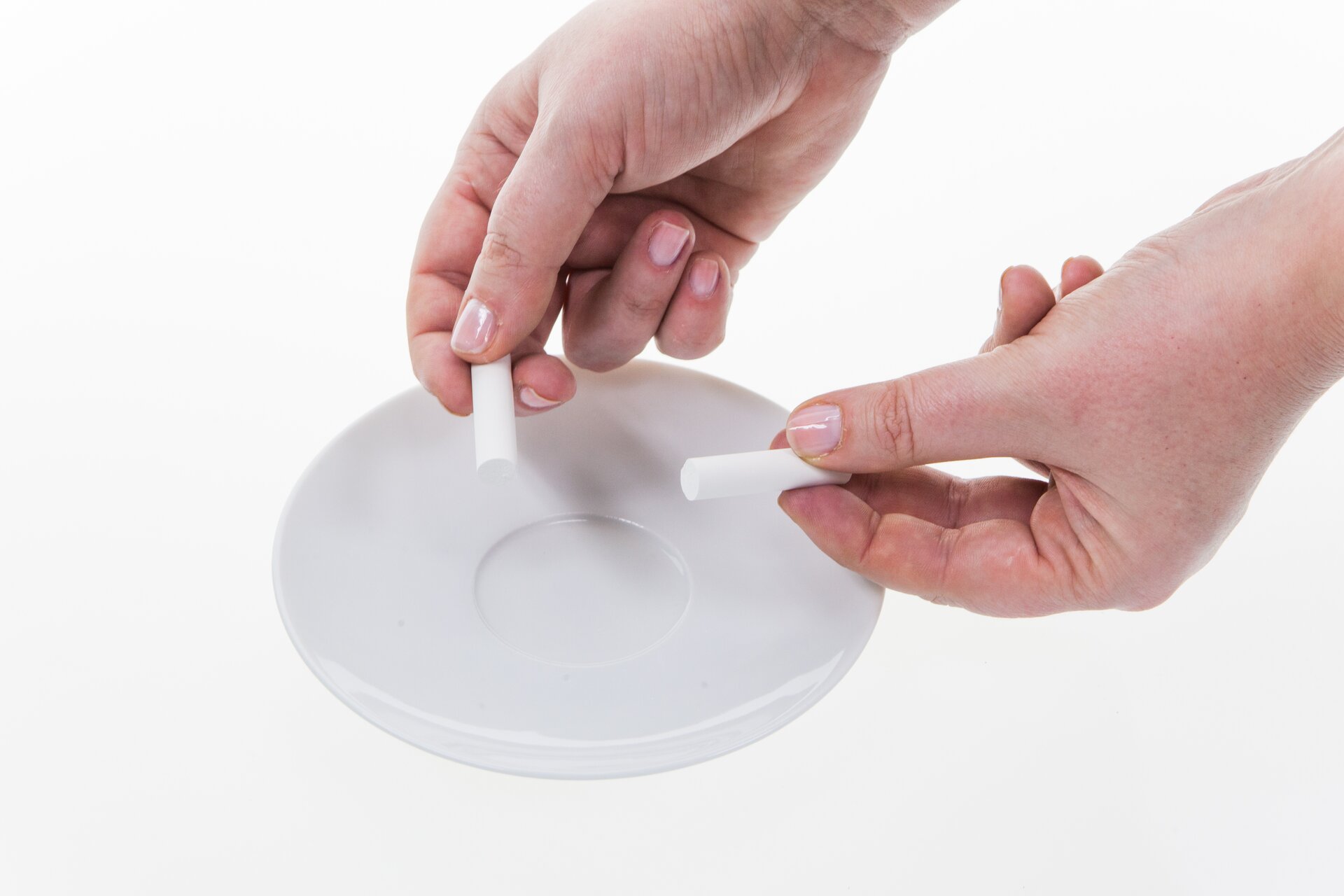 Na fotografii przedstawiono dłonie człowieka, który trzyma dwa kawałki kredy nad talerzykiem. Kreda to przykład substancji kruchej, która łatwo się łamie.