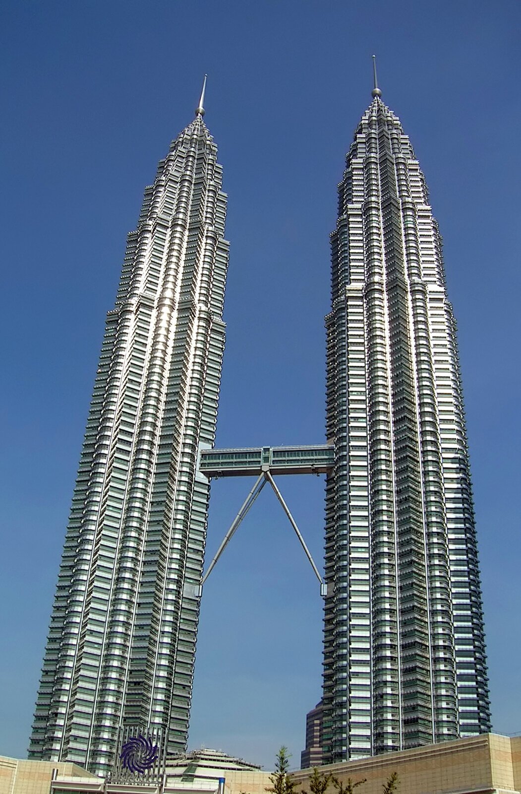 Zdjęcie przedstawia budynek Petronas Towers w Kuala Lumpur, bliźniaczych wież o wysokości czterystu pięćdziesięciu dwóch metrów. Oszklone drapacze chmur połączone są mostem o długości prawie sześćdziesięciu metrów na poziomie czterdziestego pierwszego i czterdziestego drugiego piętra.