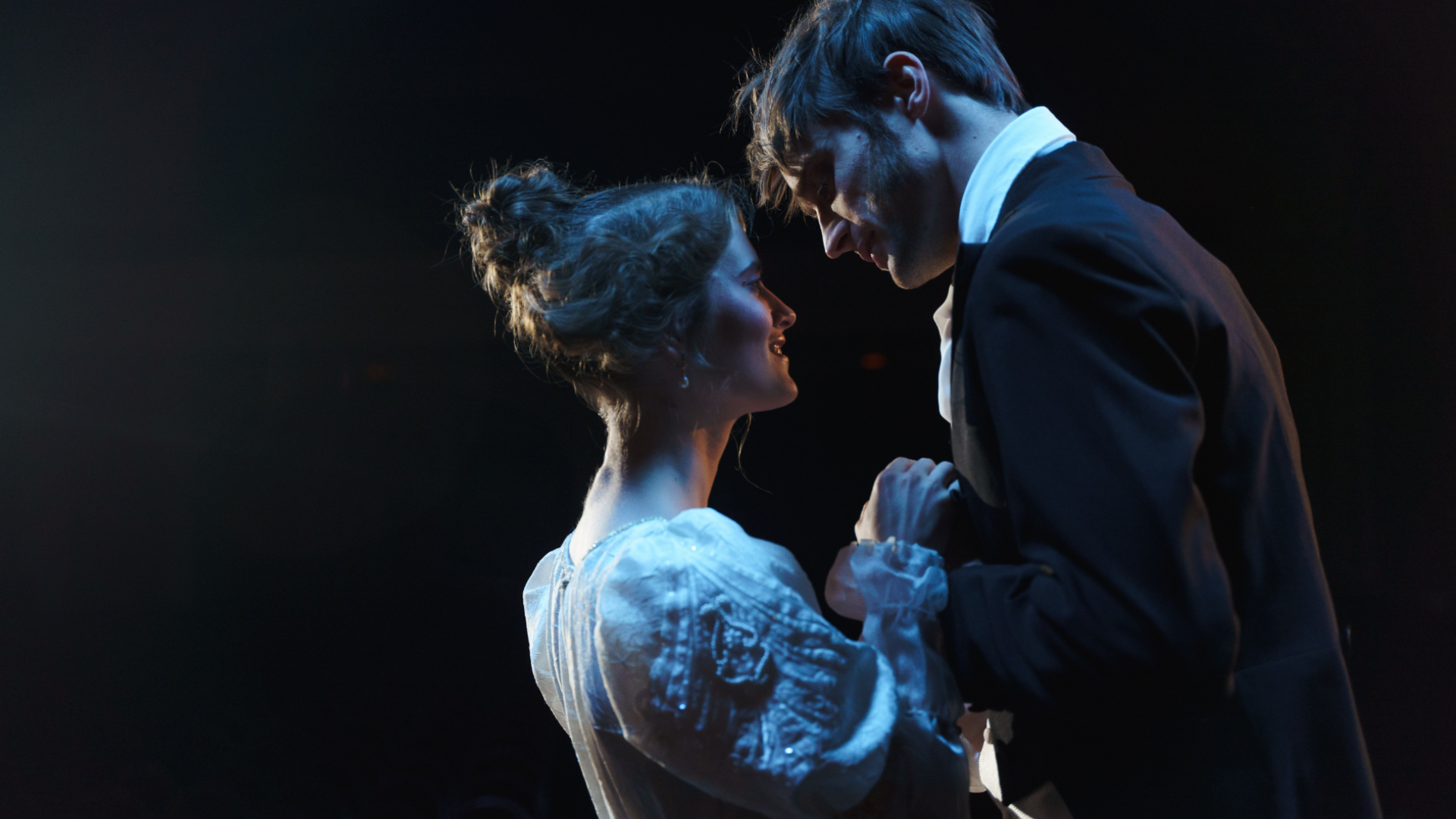 Zdjęcie przedstawia kobietę i mężczyznę (aktorkę i aktora) w trakcie spektaklu. Para stoi blisko siebie, patrzą sobie w oczy. Mają na sobie kostiumy. 