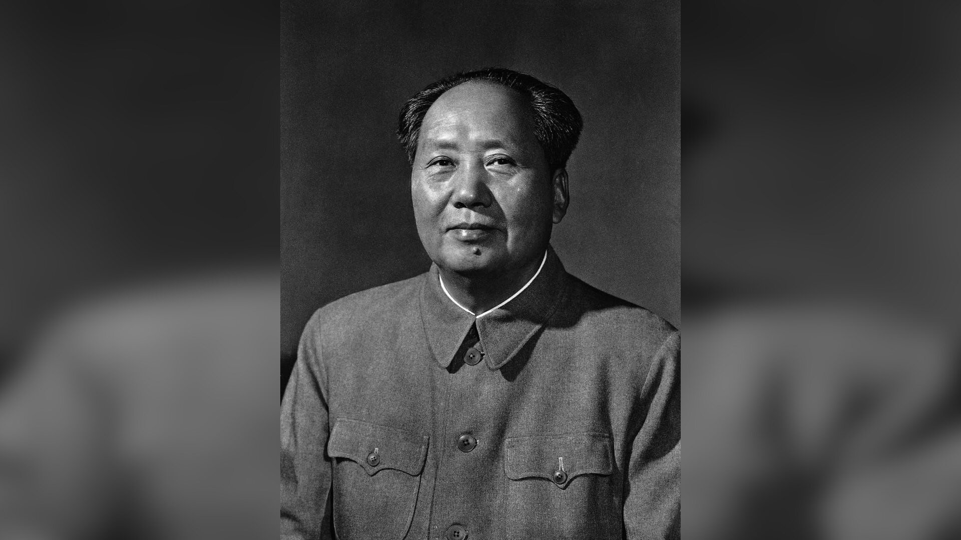 Zdjęcie przedstawia starszego mężczyznę rasy azjatyckiej. Mężczyzna ma okrągłą twarz. Jego włosy są krótkie. Mężczyzna jest lekko łysiejący. Pod dolną wargą ma brodawkę. Mężczyzna jest ubrany w prosty strój przypominający mundur.