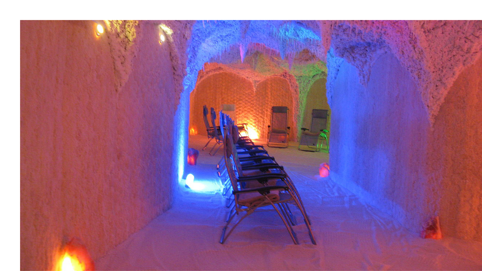 Zdjęcie przedstawia rząd krzeseł ustawionych w kolorowo oświetlonej grocie solnej.
